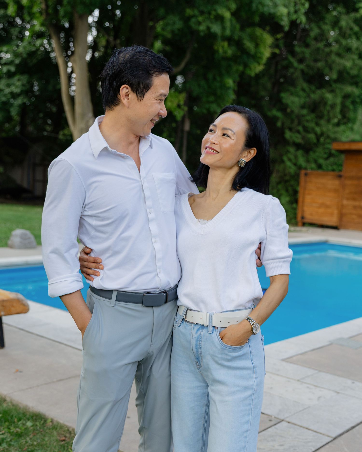 Couple in matching light outfits share joyful moments by a swimming pool.
