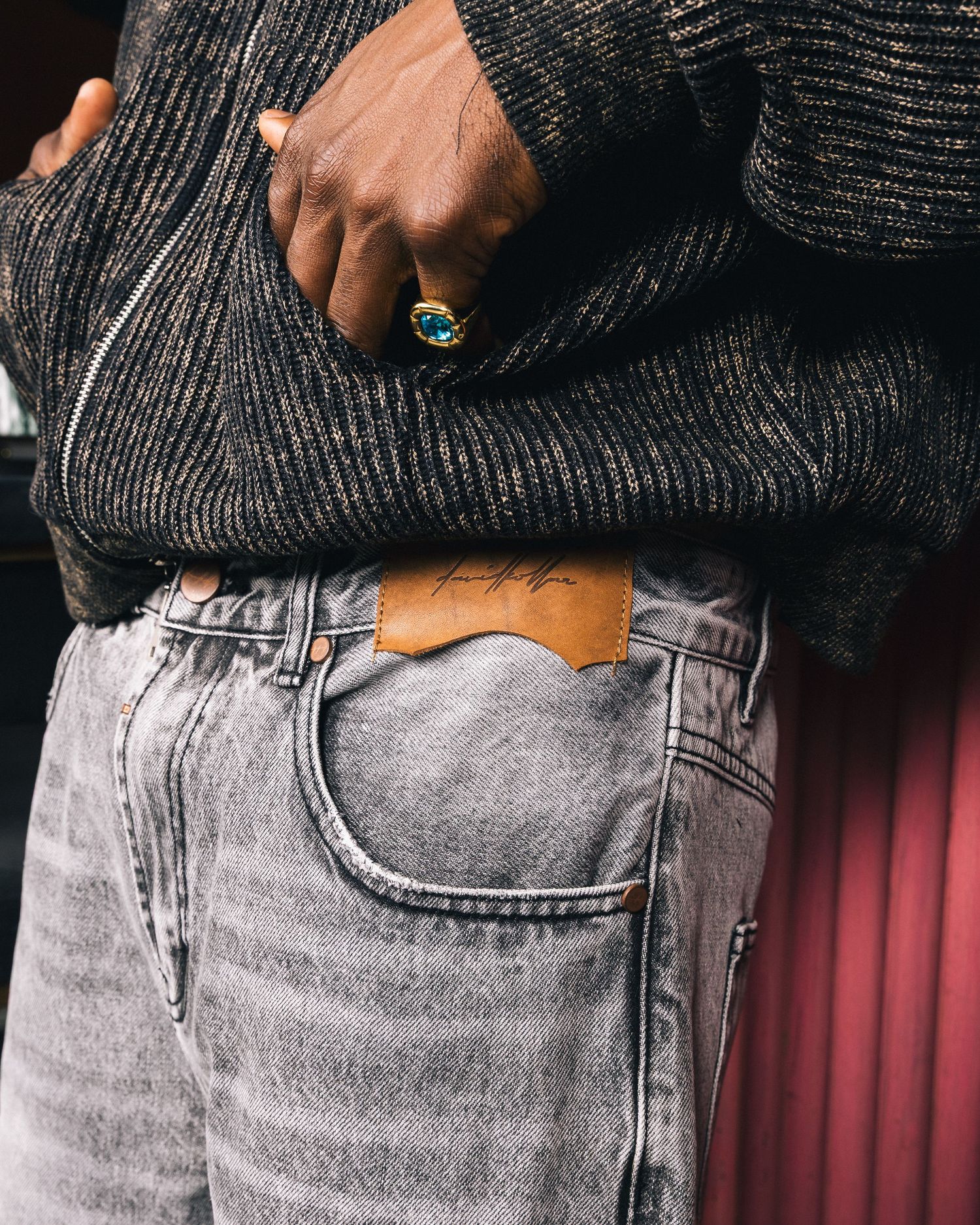 Detail shot of gray jeans with pockets against pink wall background.