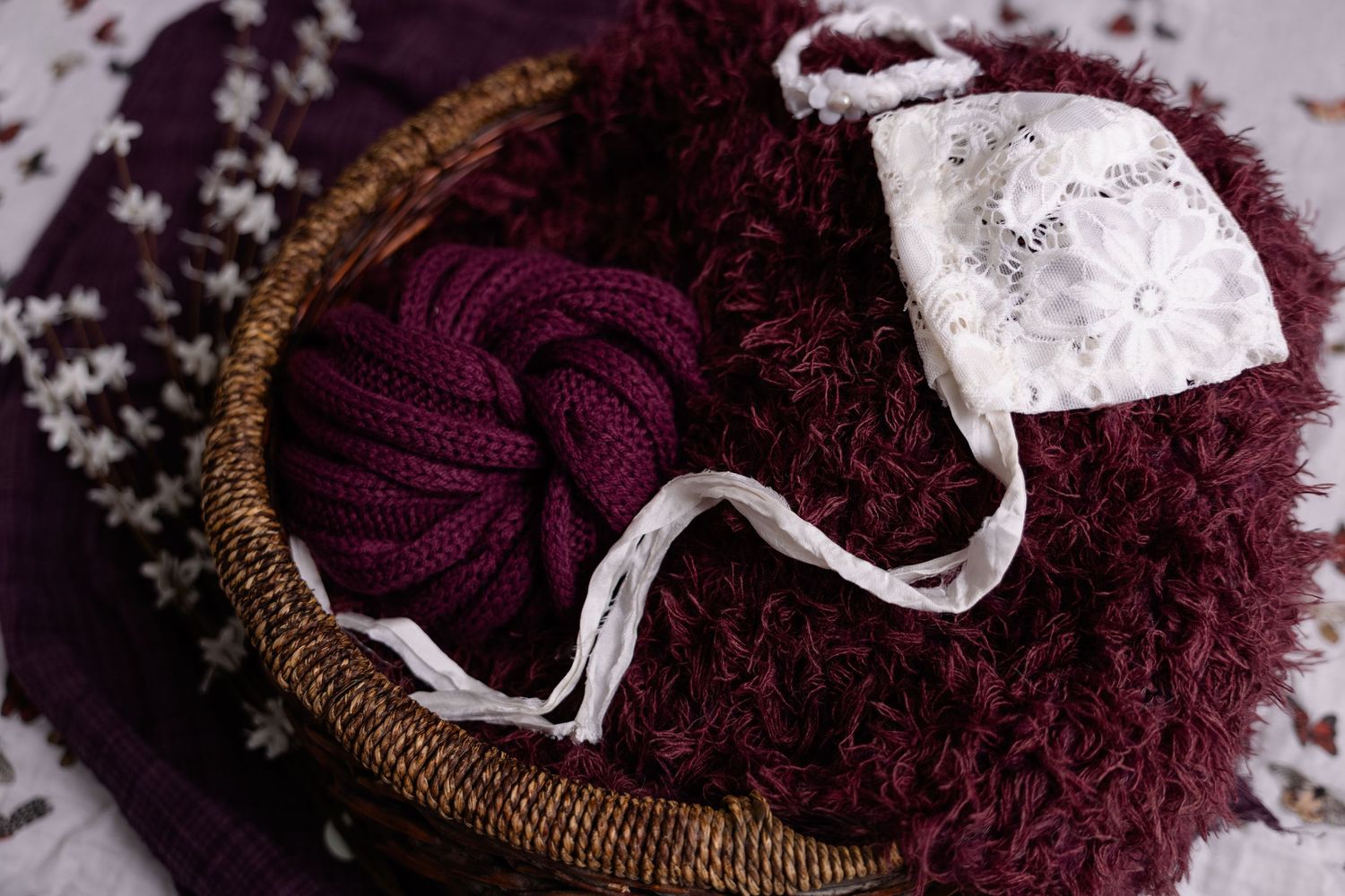 Burgundy knit wrap and white lace ribbon arranged in a rustic woven basket.