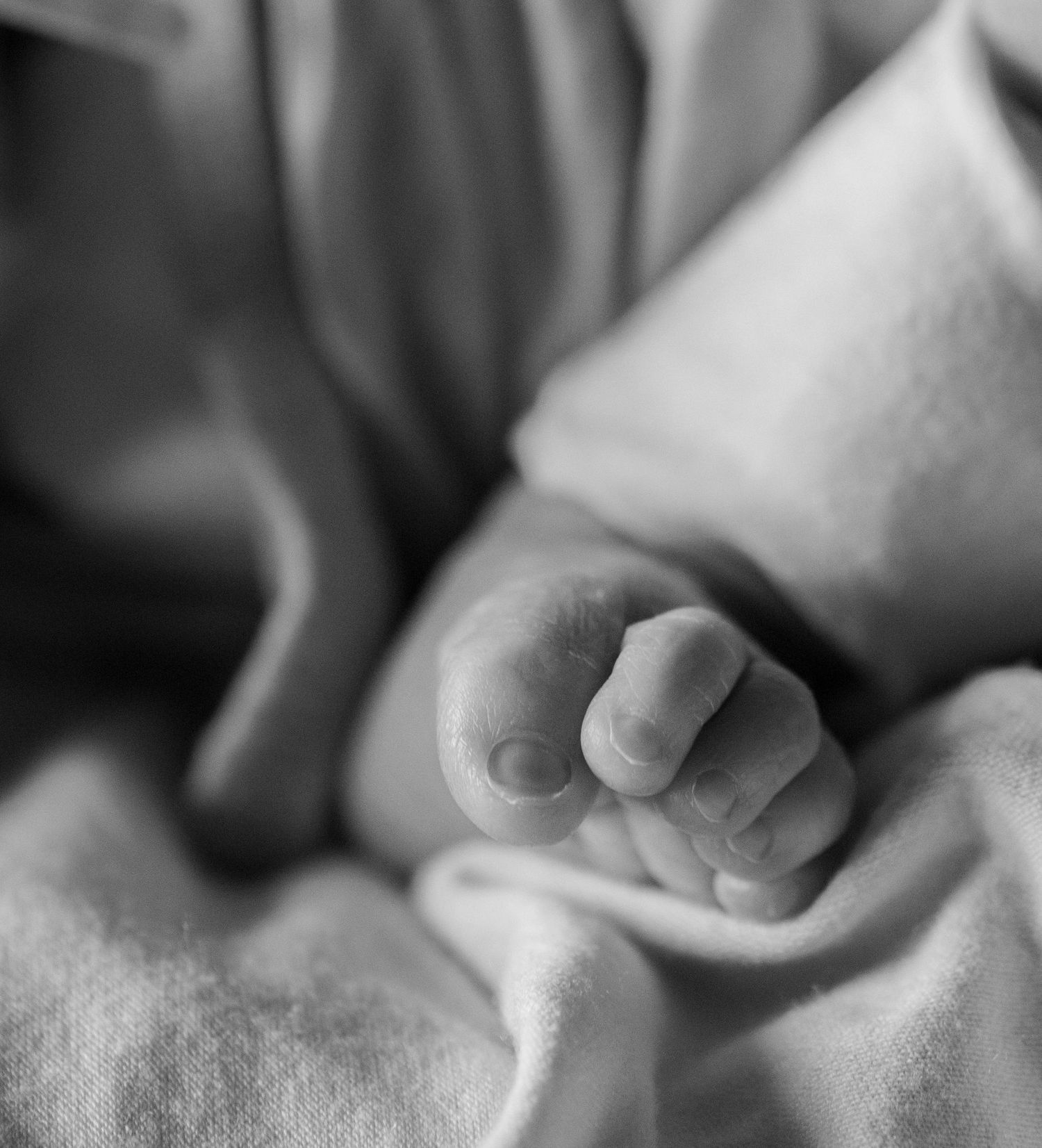 Close-up black and white photo of a newborn baby's tiny hand and toes resting on soft fabric.
