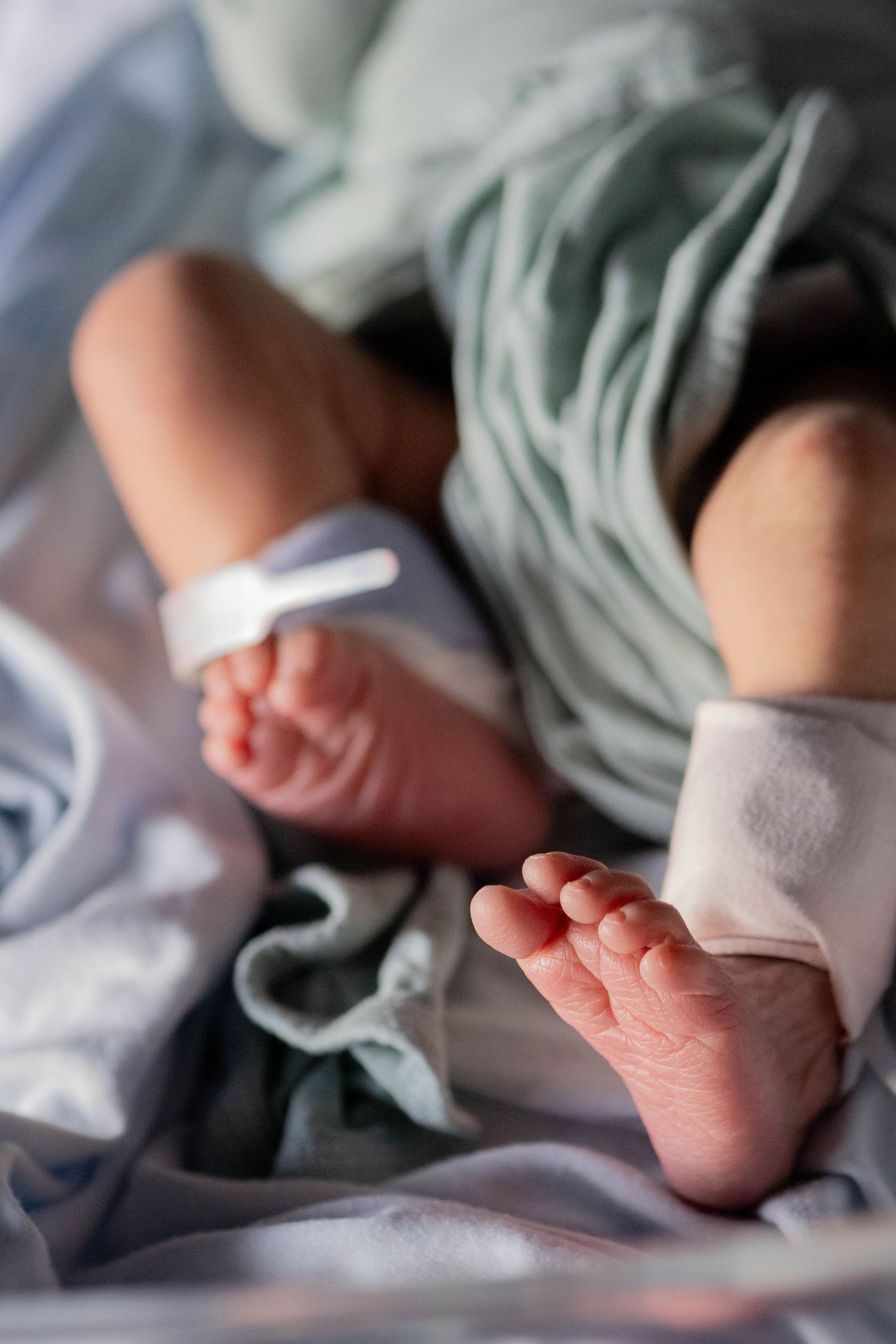 Close-up of newborn baby feet with hospital identification tags on soft blue blankets in a maternity ward.