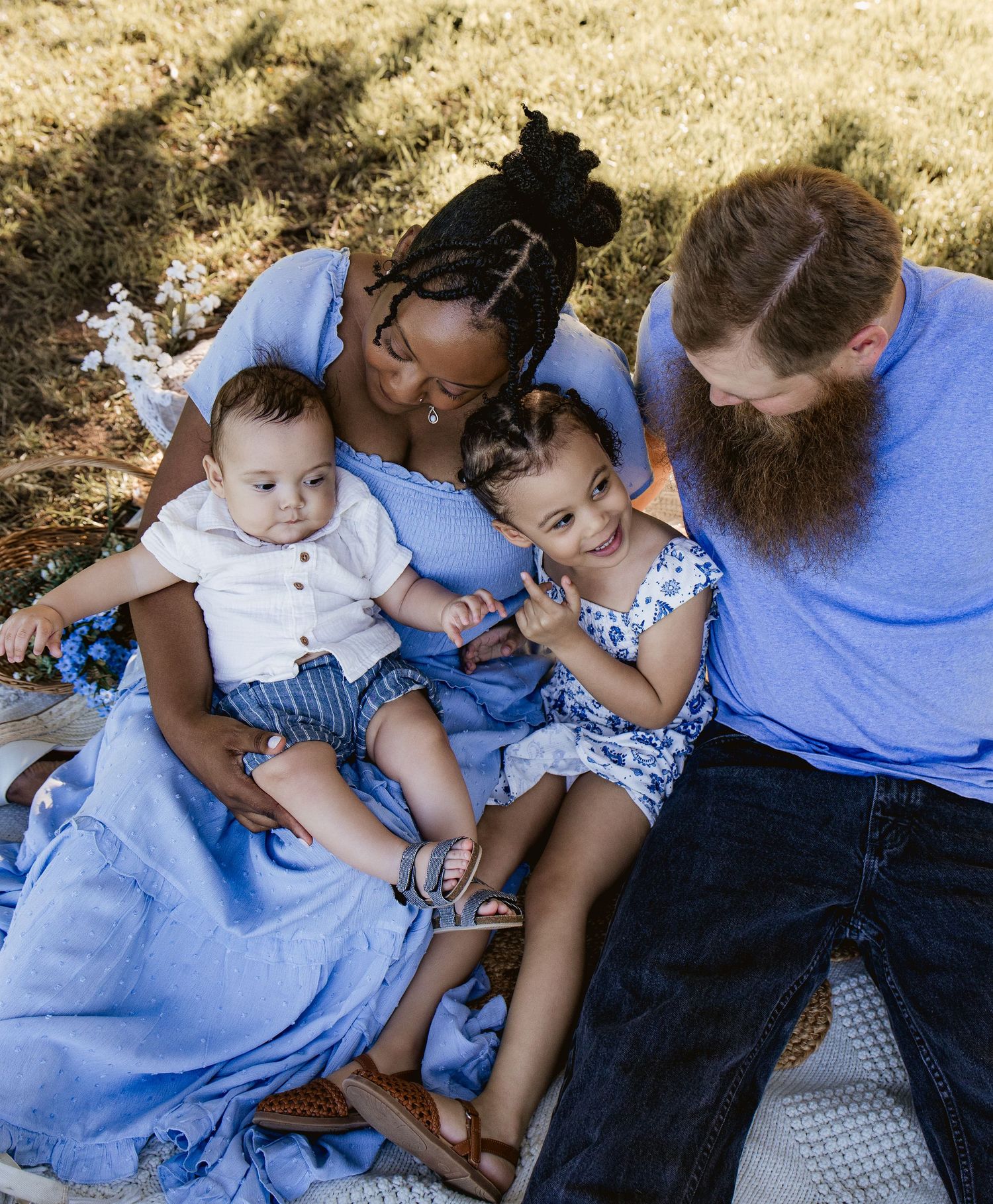 A loving interracial family of four sits on a blanket outdoors, dressed in coordinating blue outfits.