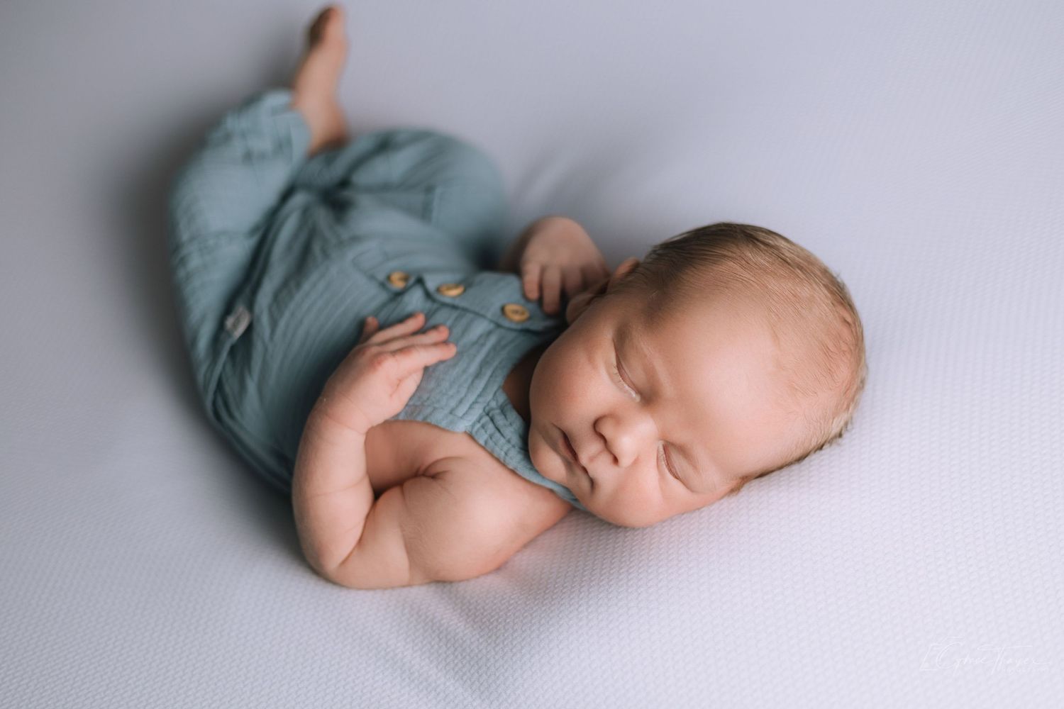 Sleeping newborn baby in teal romper lying on soft gray blanket in professional newborn photography session.