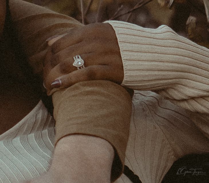 Close-up of hands with a decorative bunny ring, wearing ribbed knit sleeves in warm neutral tones.