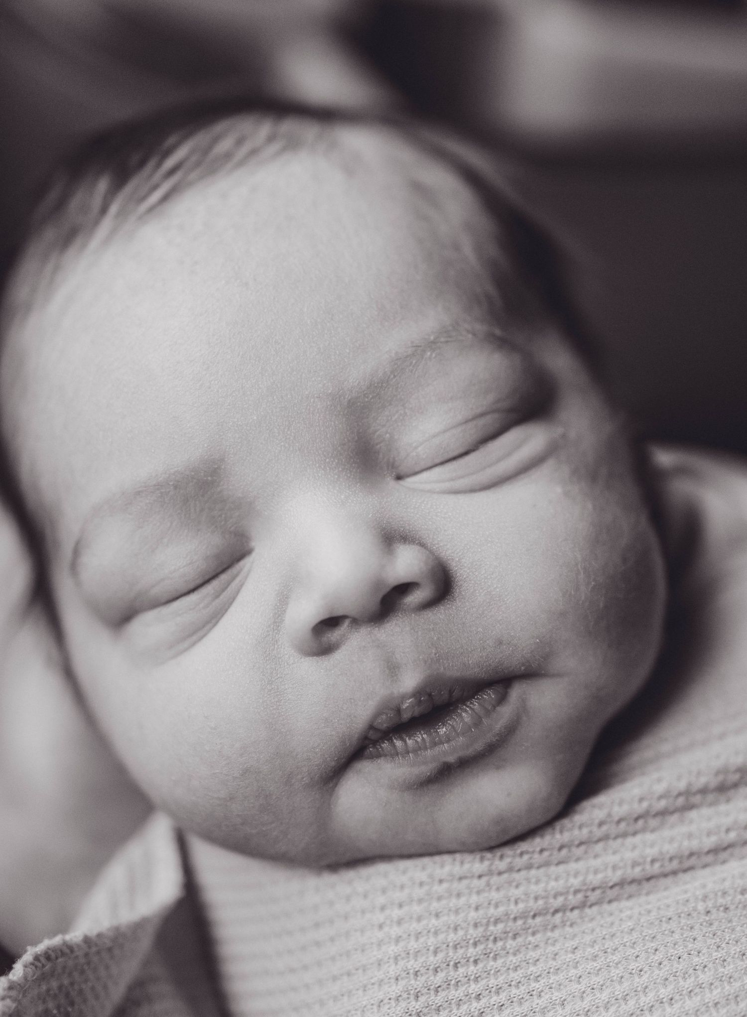 Black and white close-up portrait of a peaceful sleeping newborn baby with soft delicate features.