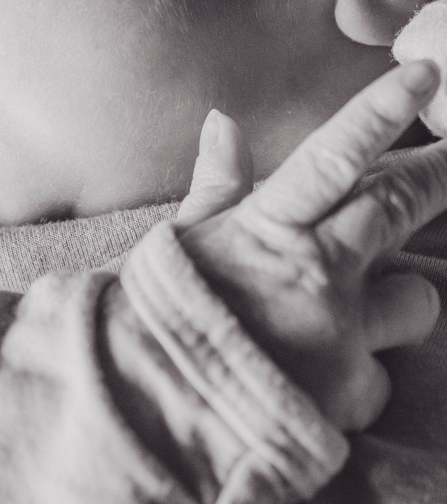 Close-up black and white photo of an adult hand gently touching a newborn baby's chest in a tender moment.
