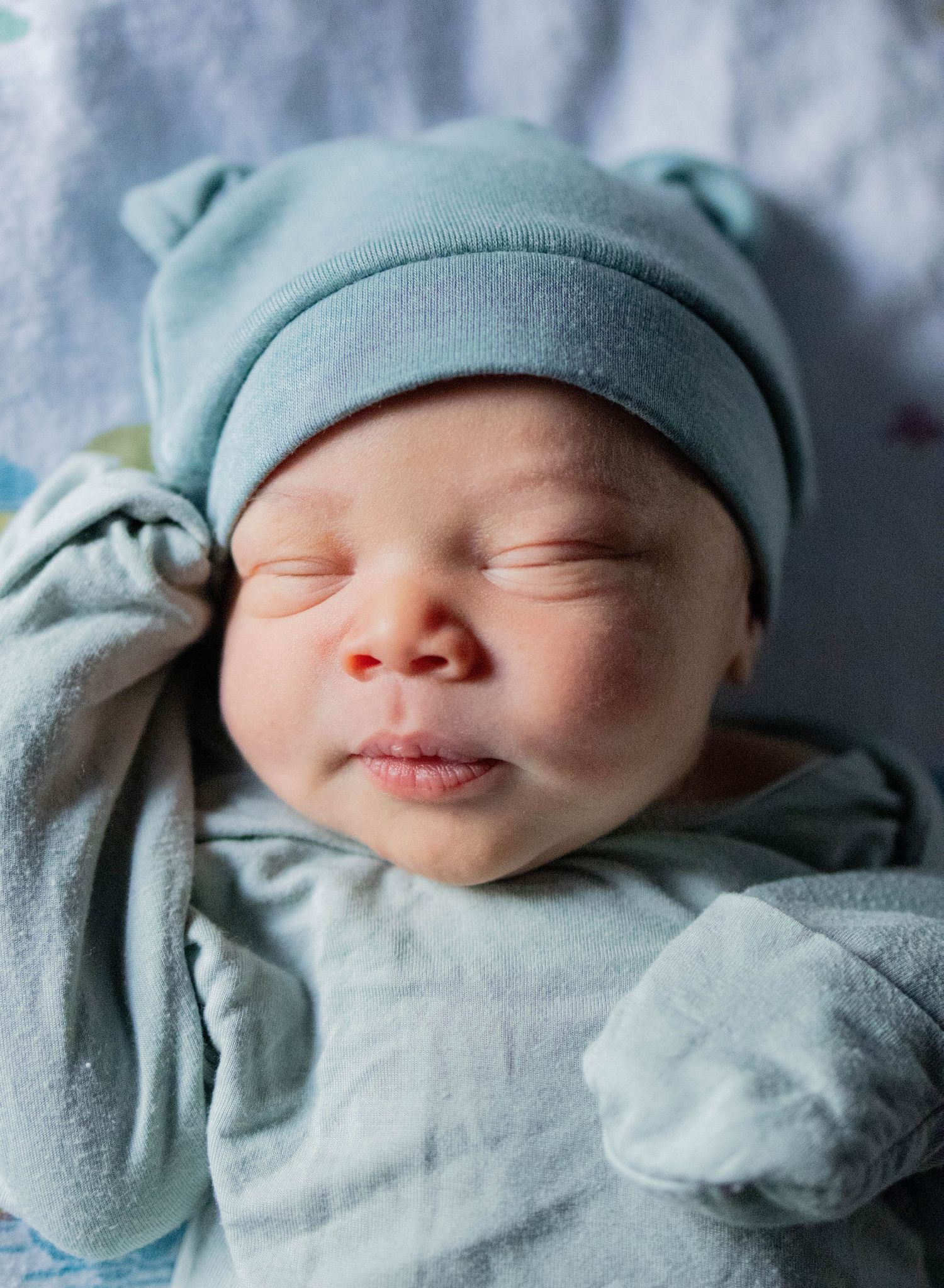 Peaceful newborn baby sleeping in a light blue hat and swaddle blanket.