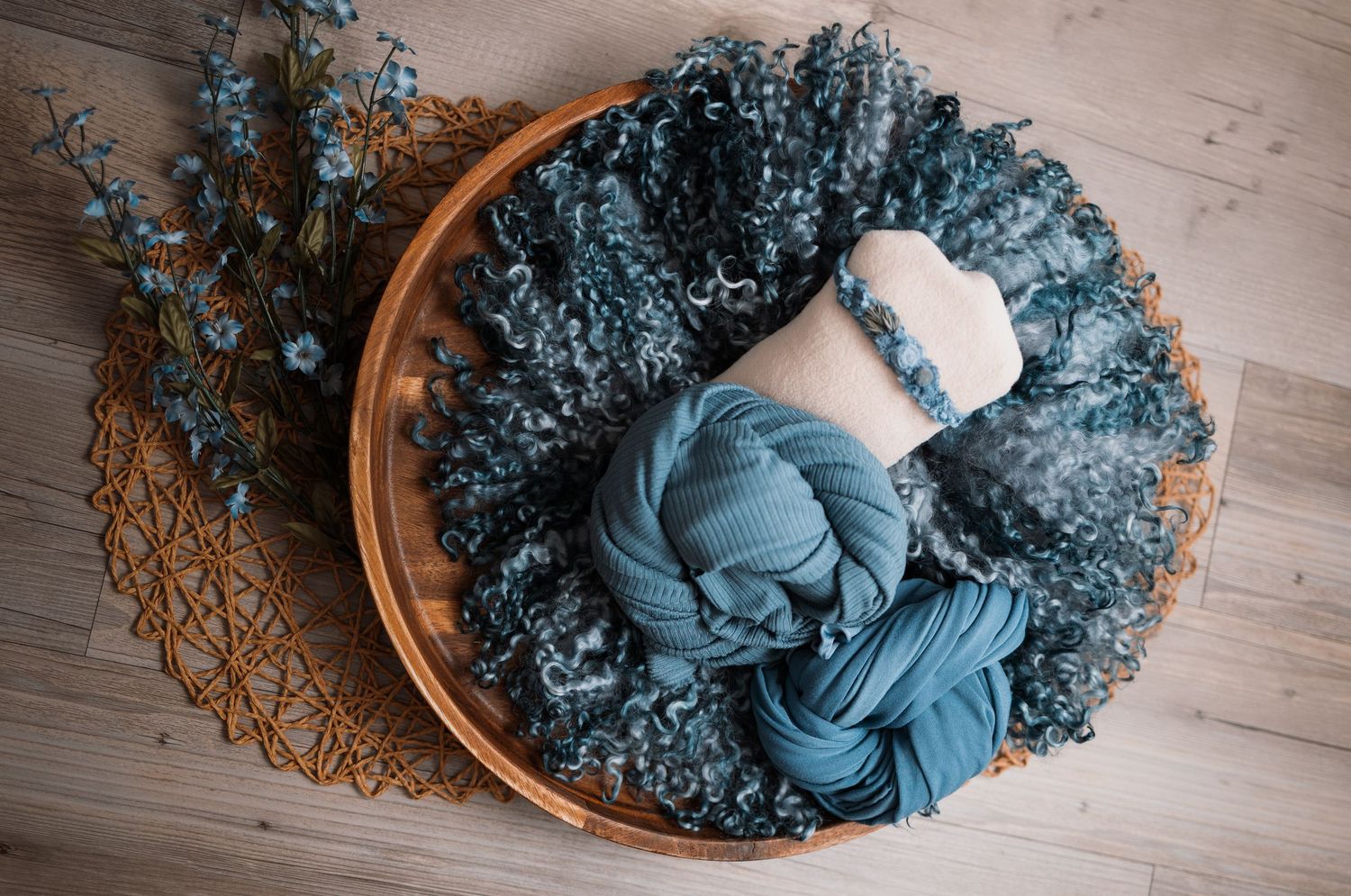 A series of newborn photography shots showing a sleeping baby in blue wrap on a wooden floor with a wicker basket.