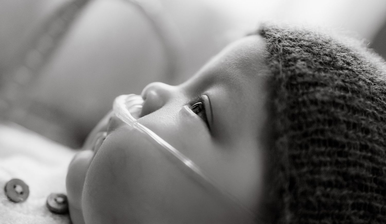 Black and white close-up portrait of a newborn baby wearing a knit hat, gazing upward with curious eyes.