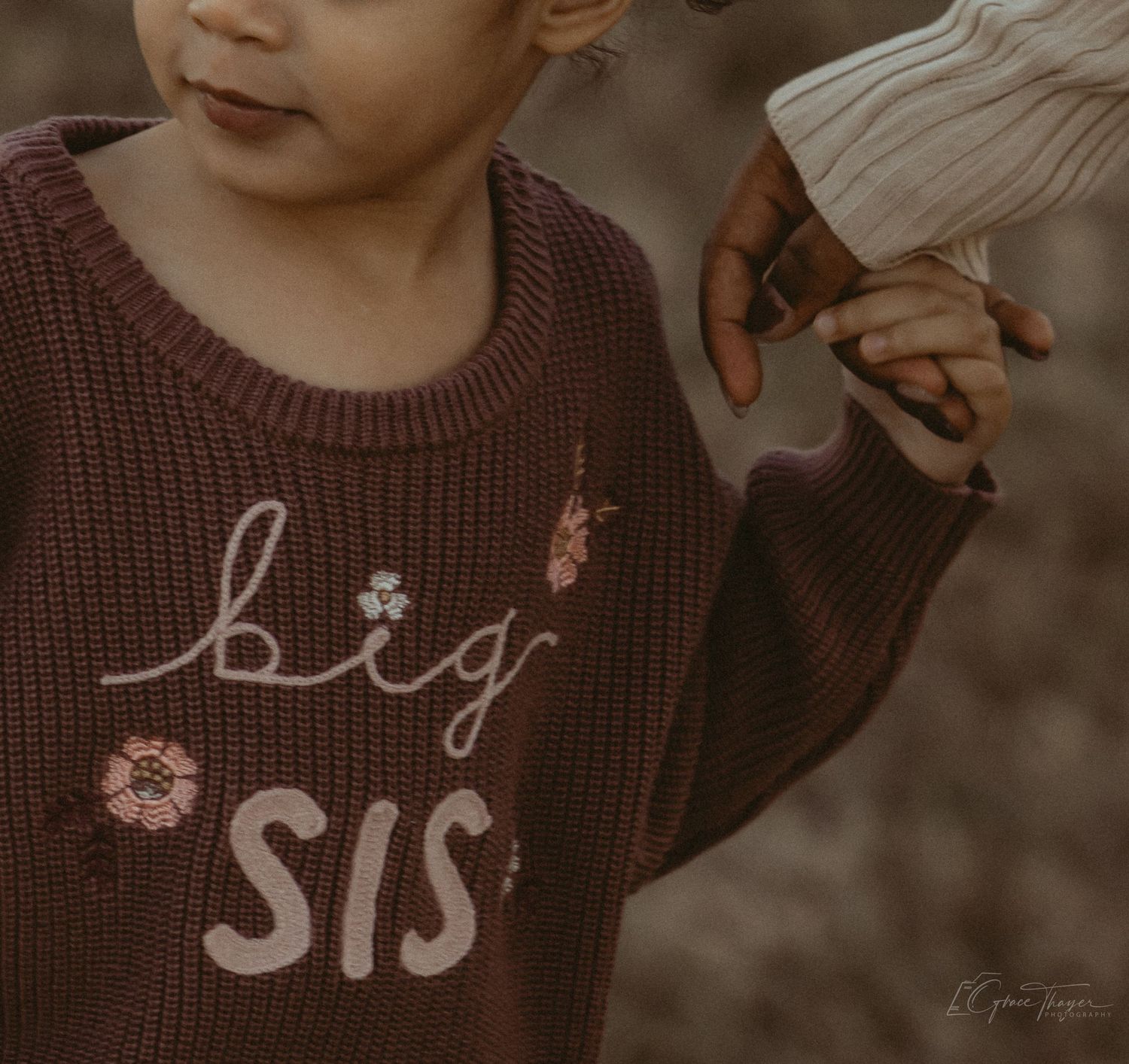 Young girl wearing a brown knit sweater embroidered with 