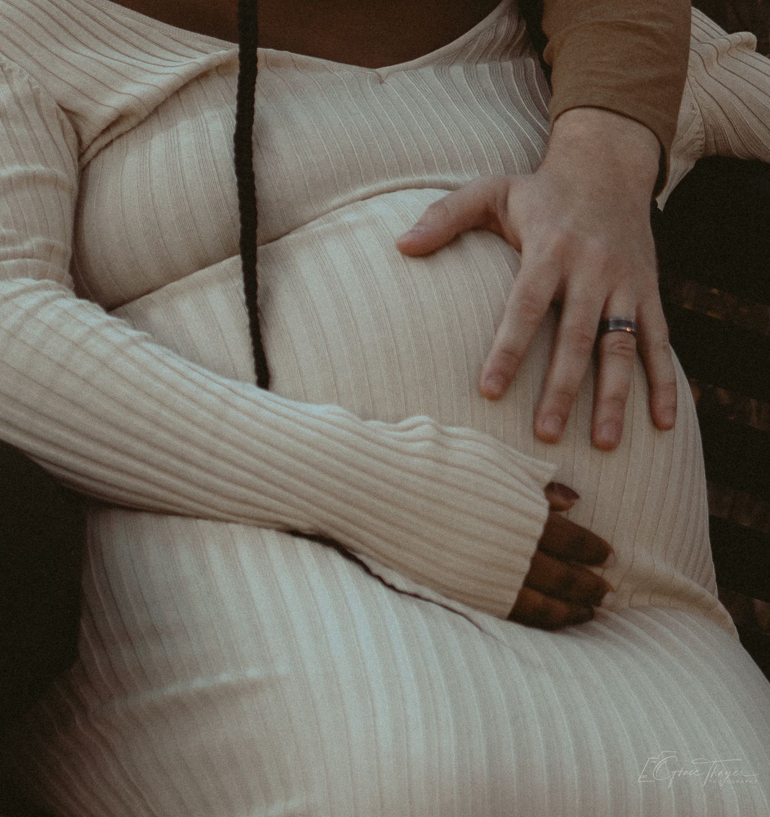 Pregnant woman in ribbed cream dress cradling baby bump with ringed hand.