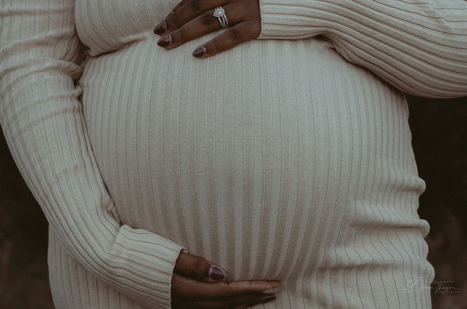 Pregnant woman in cream ribbed dress cradling baby bump, showcasing maternity fashion and pregnancy glow.
