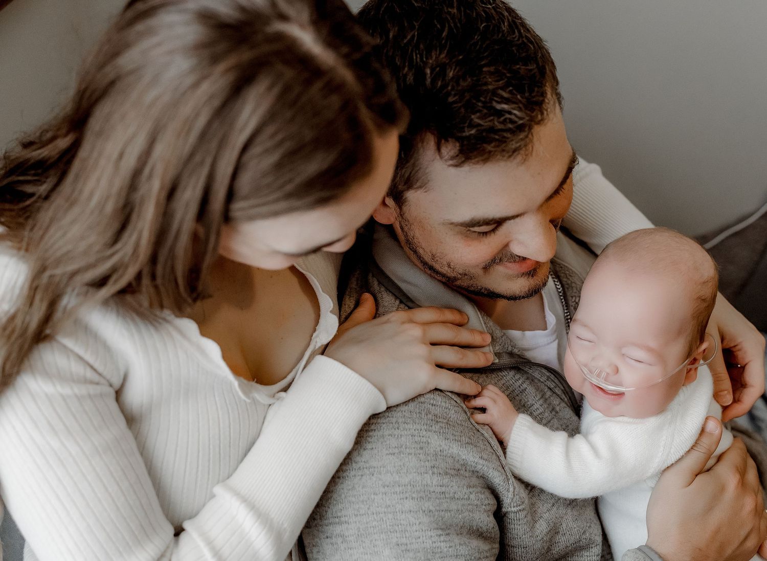 A couple lovingly gazes at their sleeping newborn baby, sharing a tender family moment together.