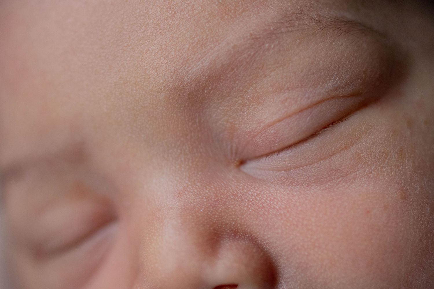 Close-up of a sleeping newborn baby's face with delicate closed eyes and soft skin.