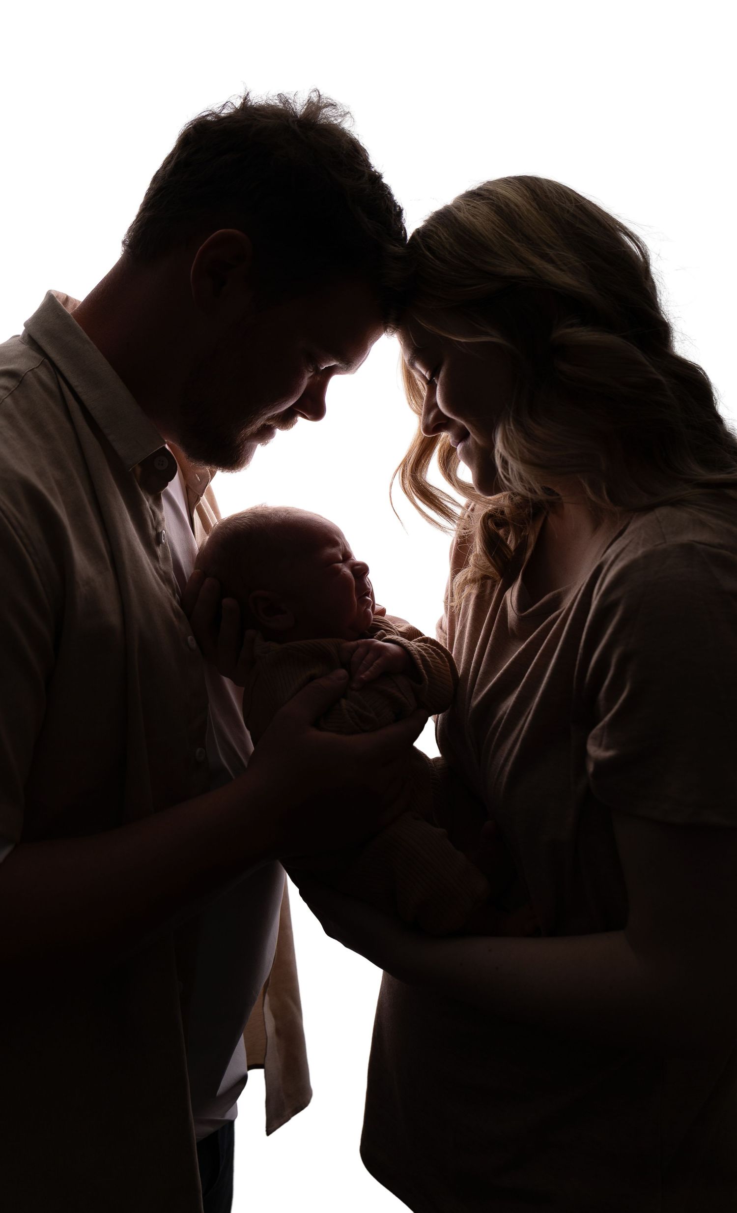 Silhouette of parents tenderly holding their newborn baby against a bright white background.