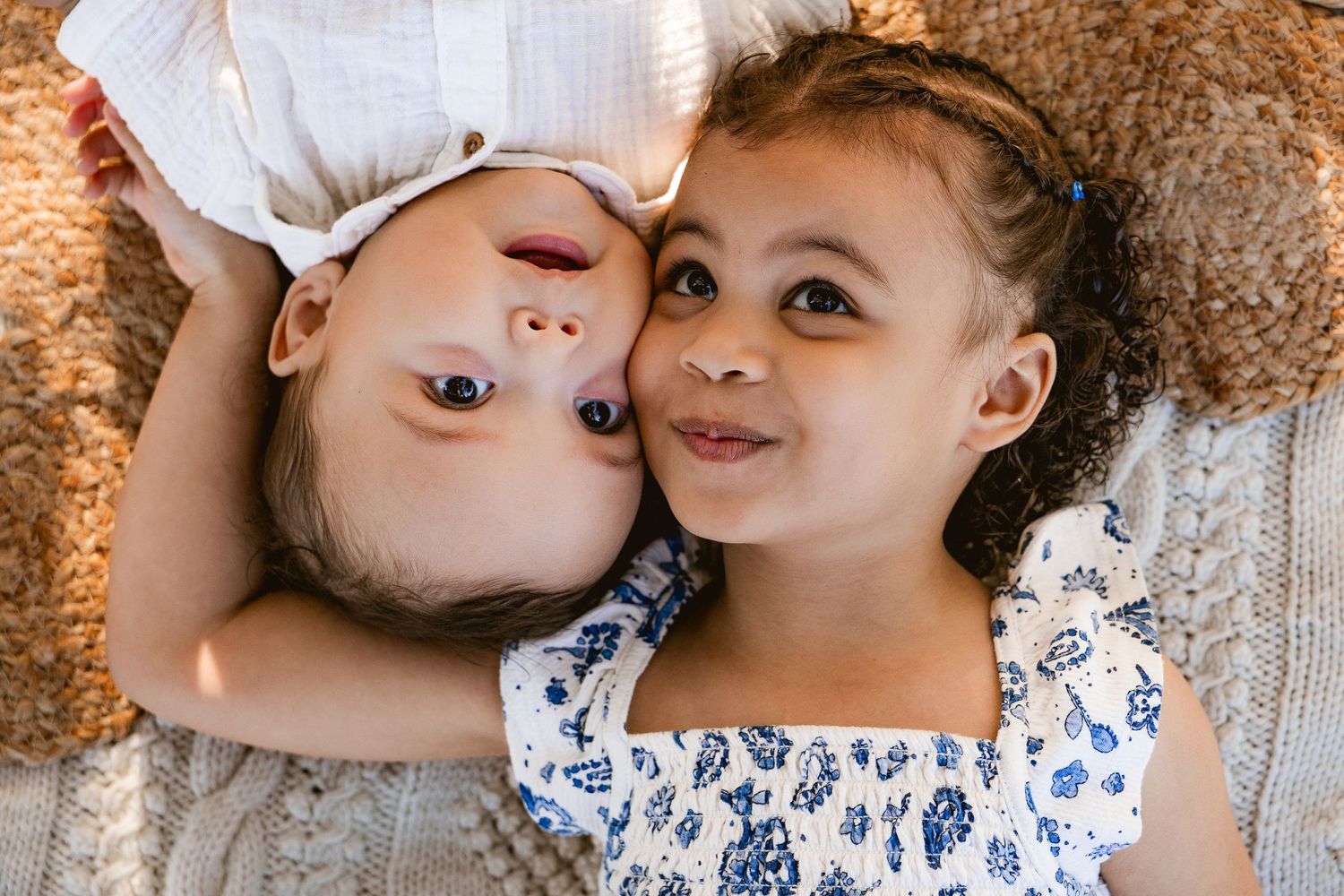 Two young girls lying on a blanket together, smiling and cuddling in a heartwarming moment.