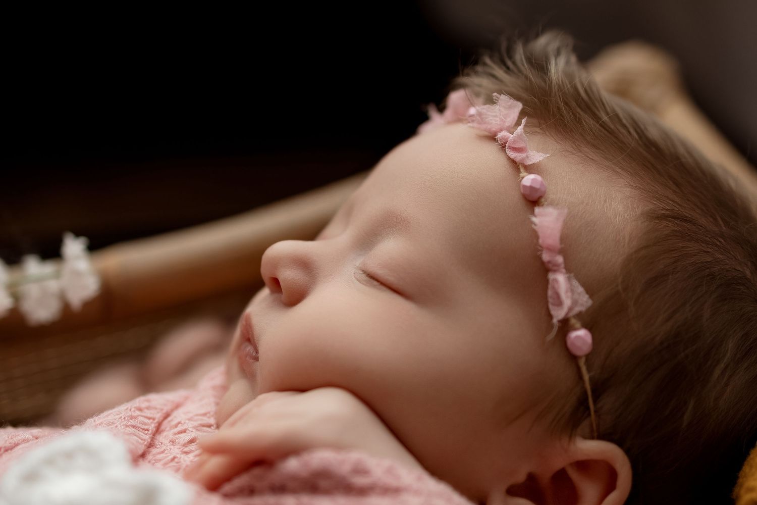 Peaceful newborn baby girl sleeping wearing a delicate pink pearl headband, wrapped in soft pink blanket.
