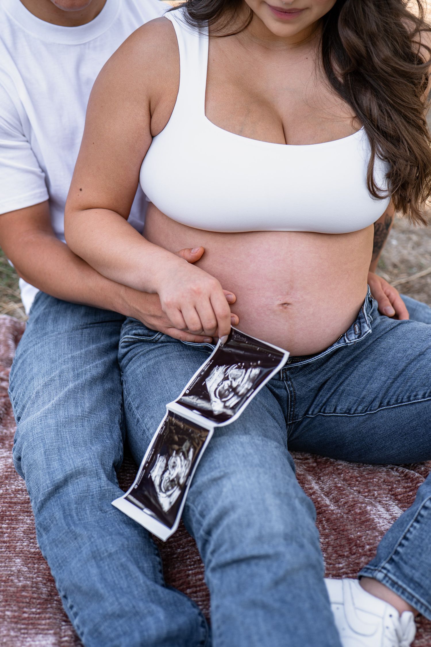 Intimate maternity photo session with ultrasound images displayed on rustic wooden bench.