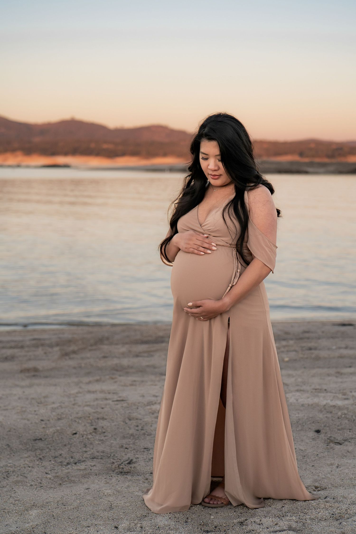 Expectant couple in neutral tones embracing on beach during sunset maternity photoshoot in Roseville, CA