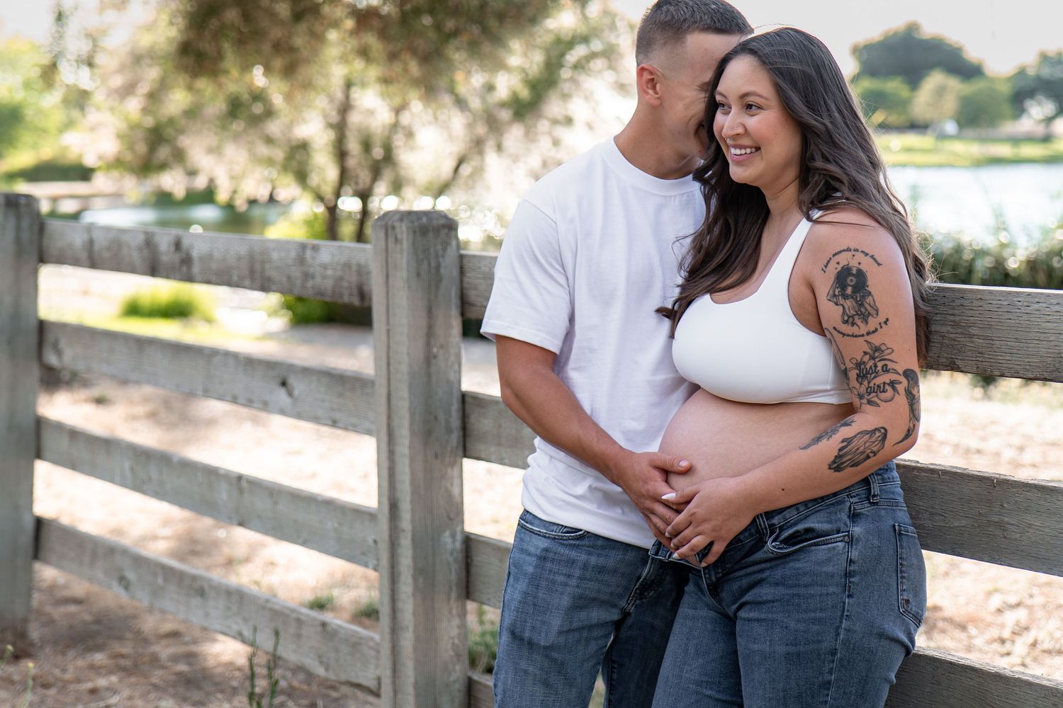 A couple embraces during a romantic outdoor photoshoot near a wooden fence.