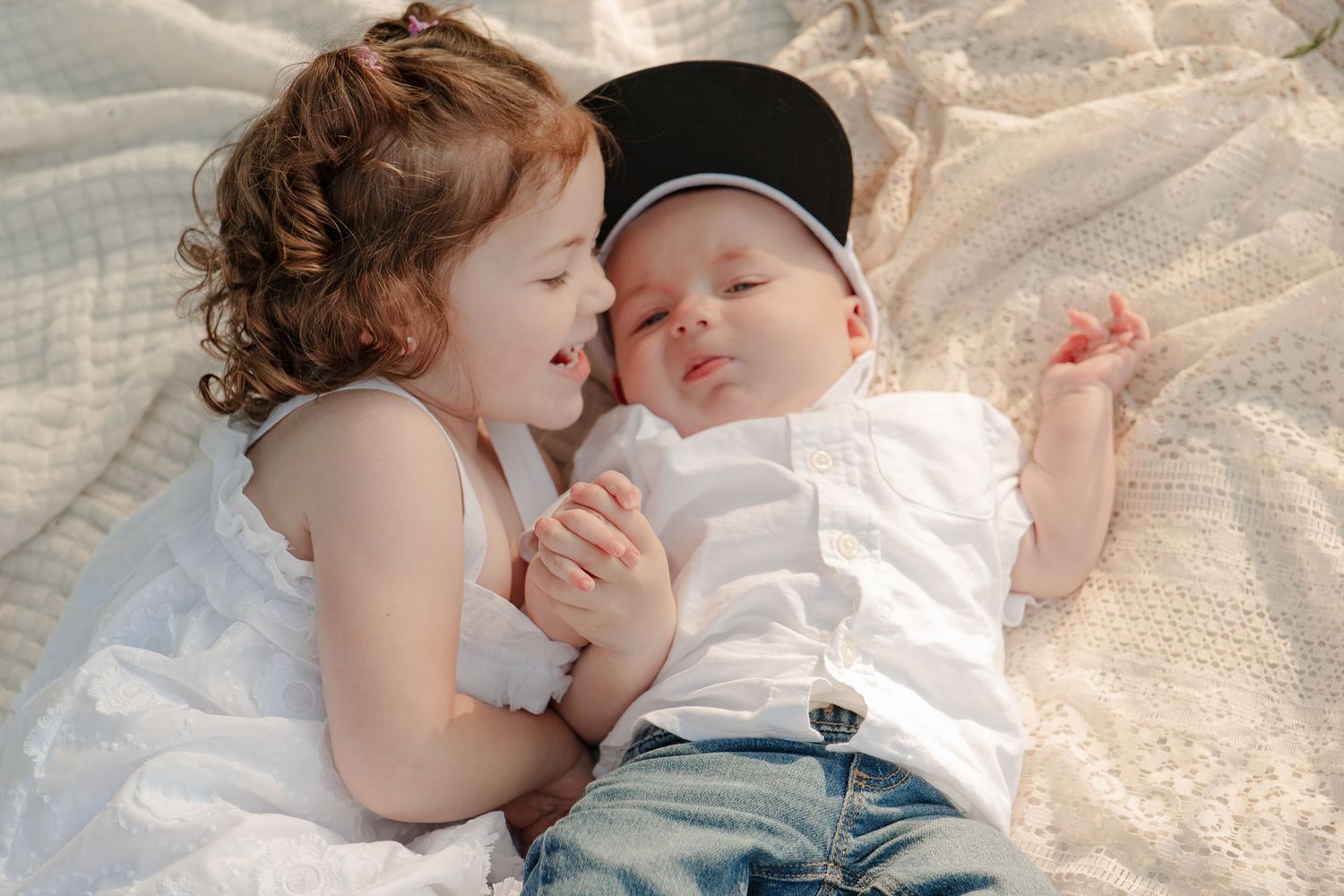 Two young children cuddling together on a white blanket in soft lighting.