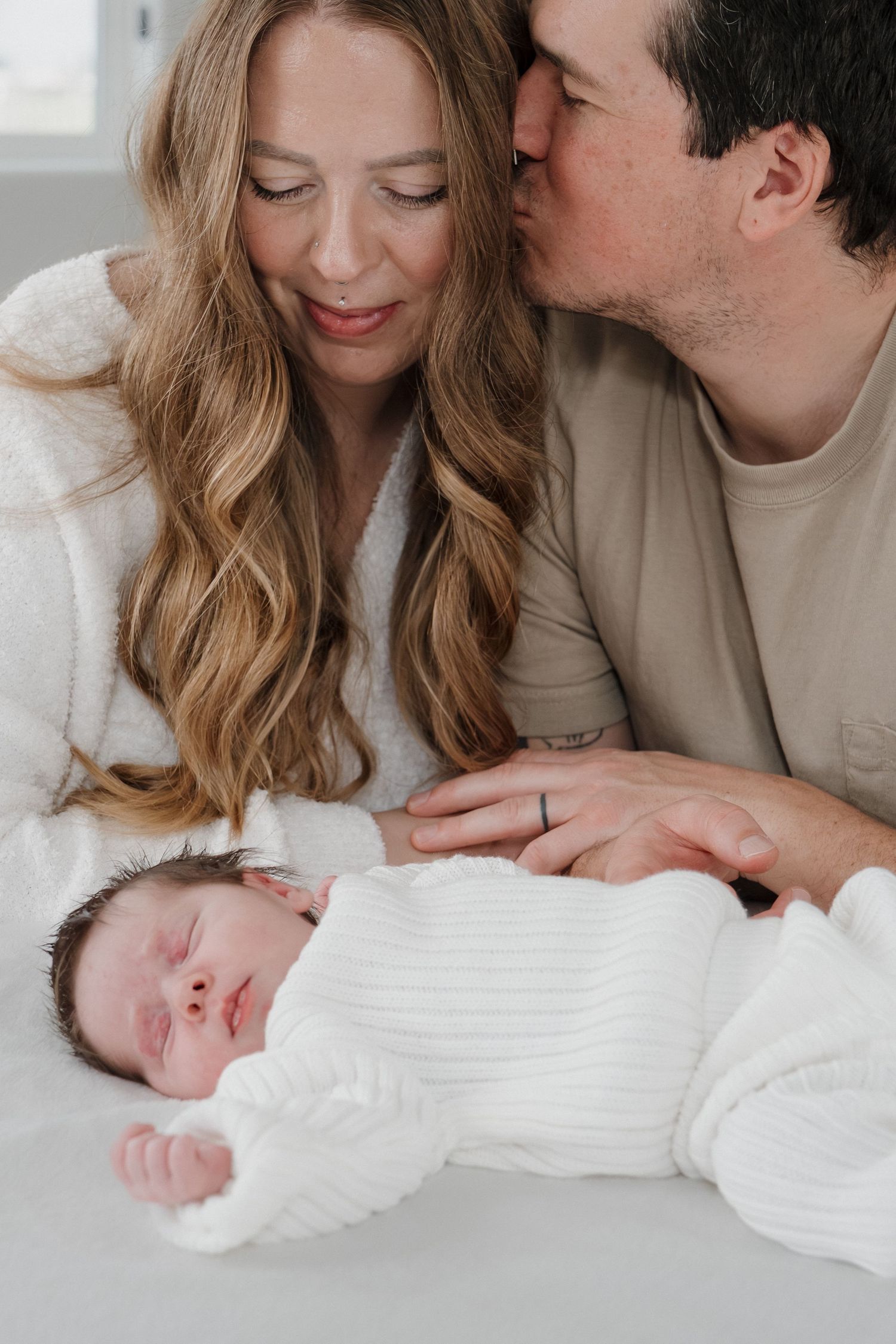 Parents admiring their newborn baby lying on white bedding in Roseville, CA