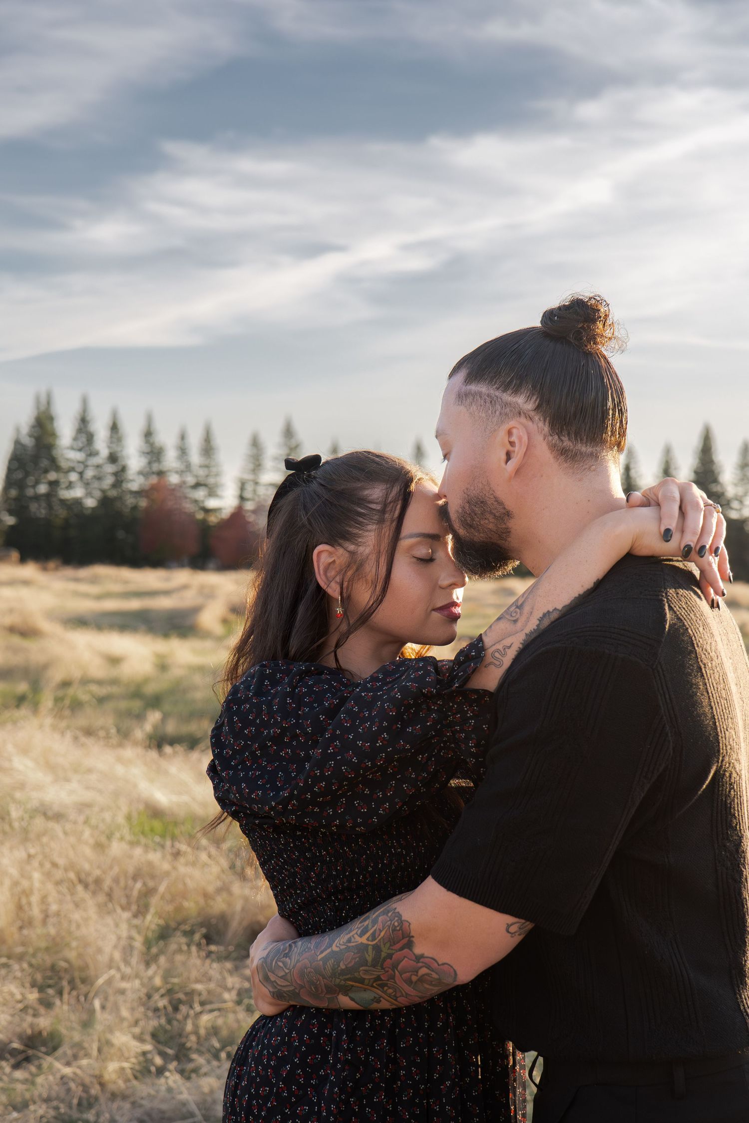 Romantic couple embracing in a golden field with evergreen trees at sunset in Roseville, CA