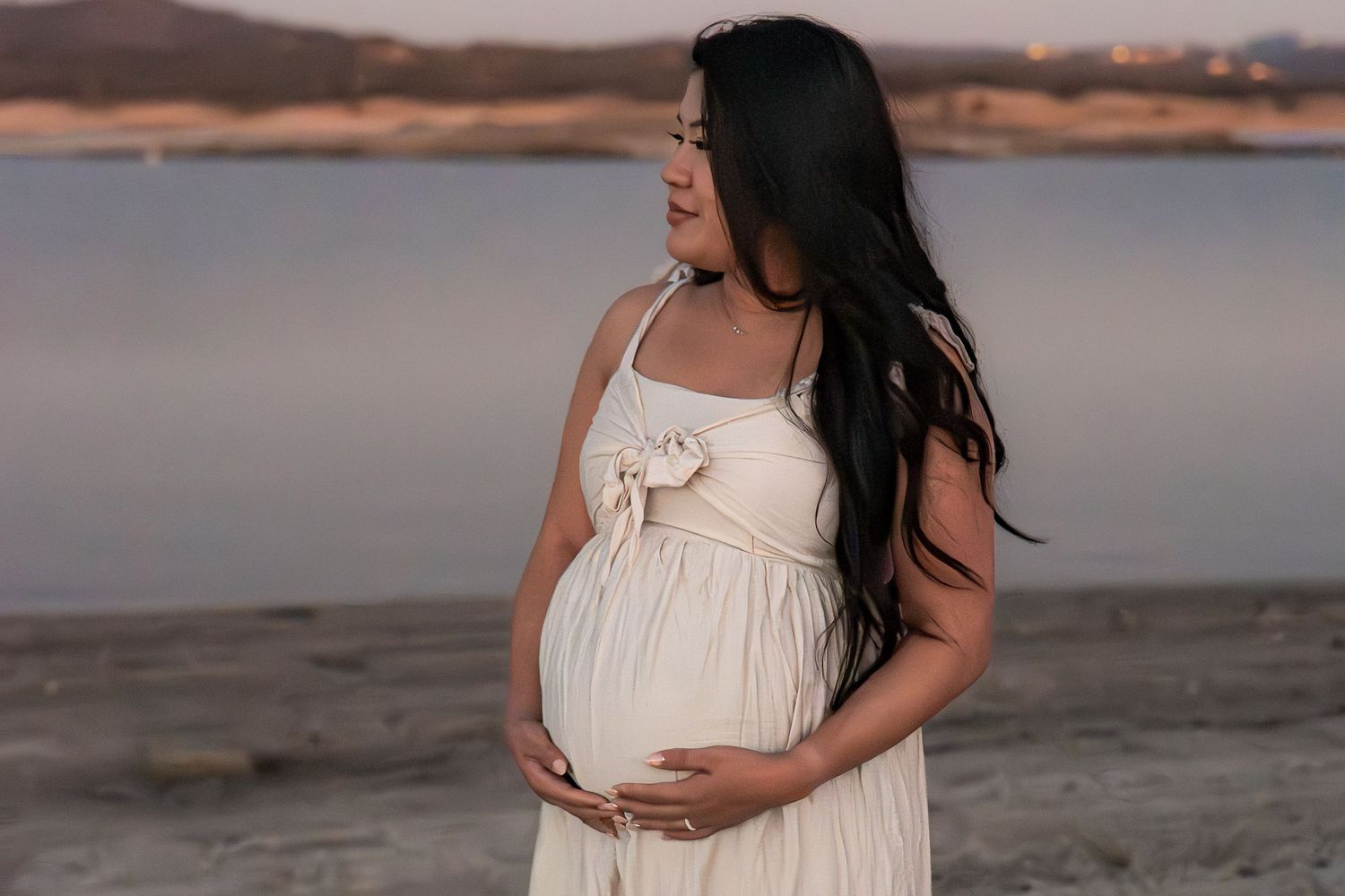Maternity photos at sunset showing woman in flowing cream dress by the water in Roseville, CA