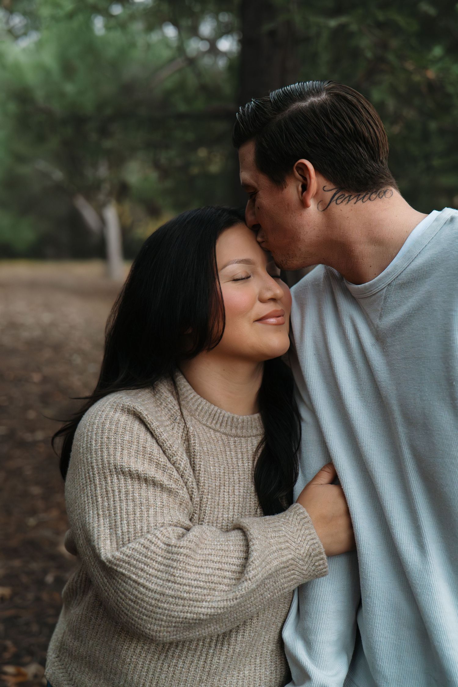 A tender moment between a couple in matching sweaters against a forest backdrop.