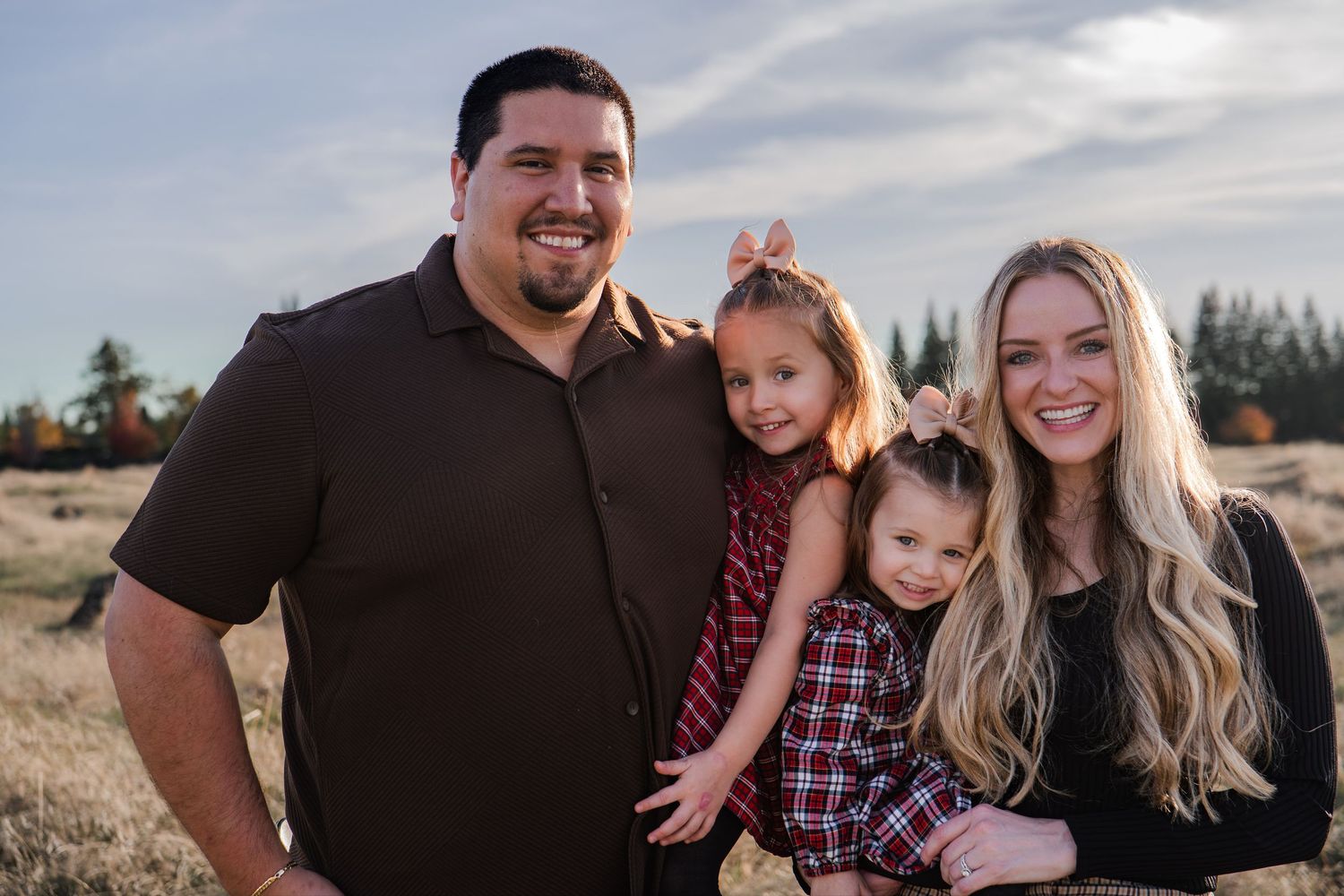 A family poses together in a field during golden hour wearing coordinating burgundy and black outfits.