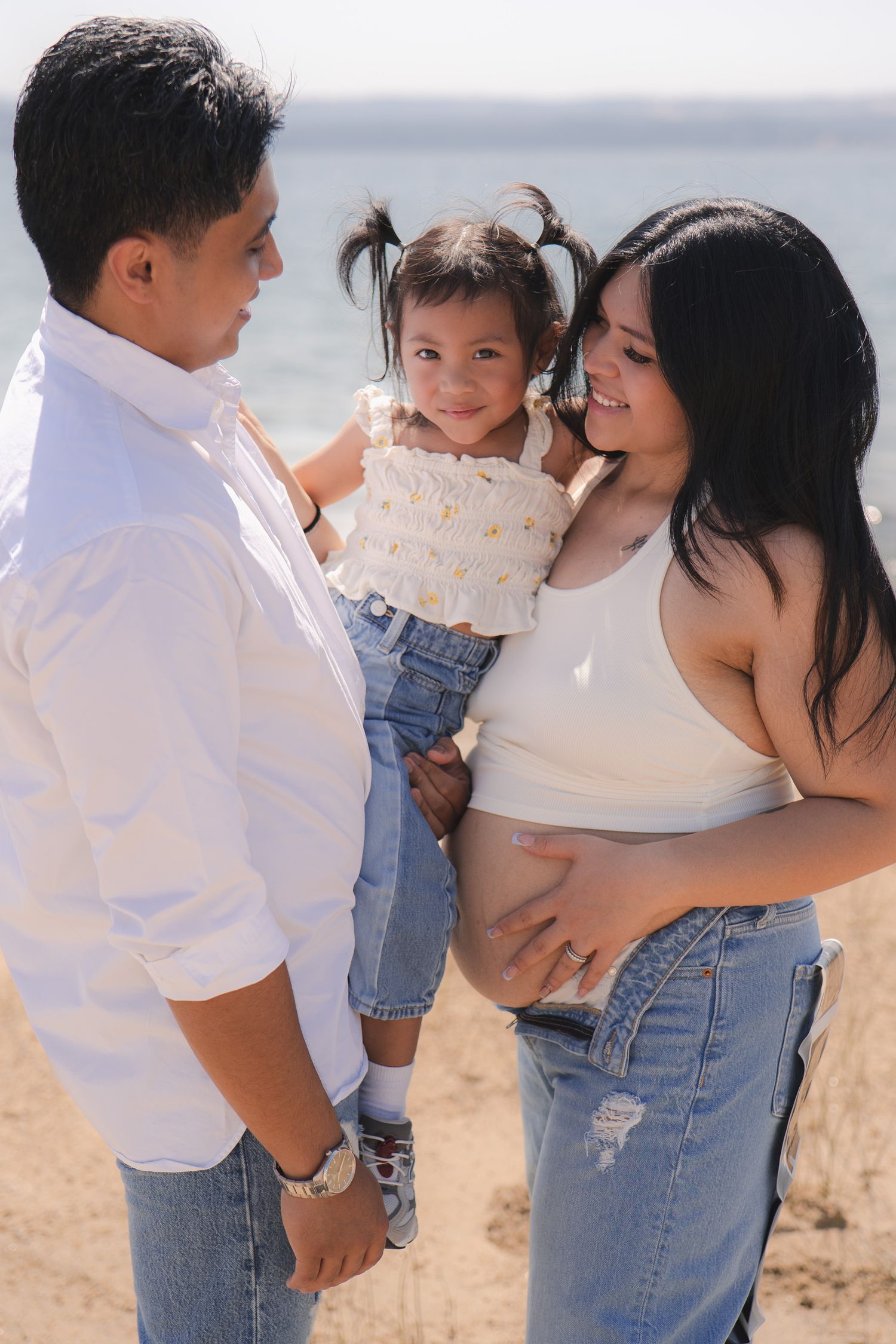 Family photo session at the beach showing tender moments in casual denim and white outfits.