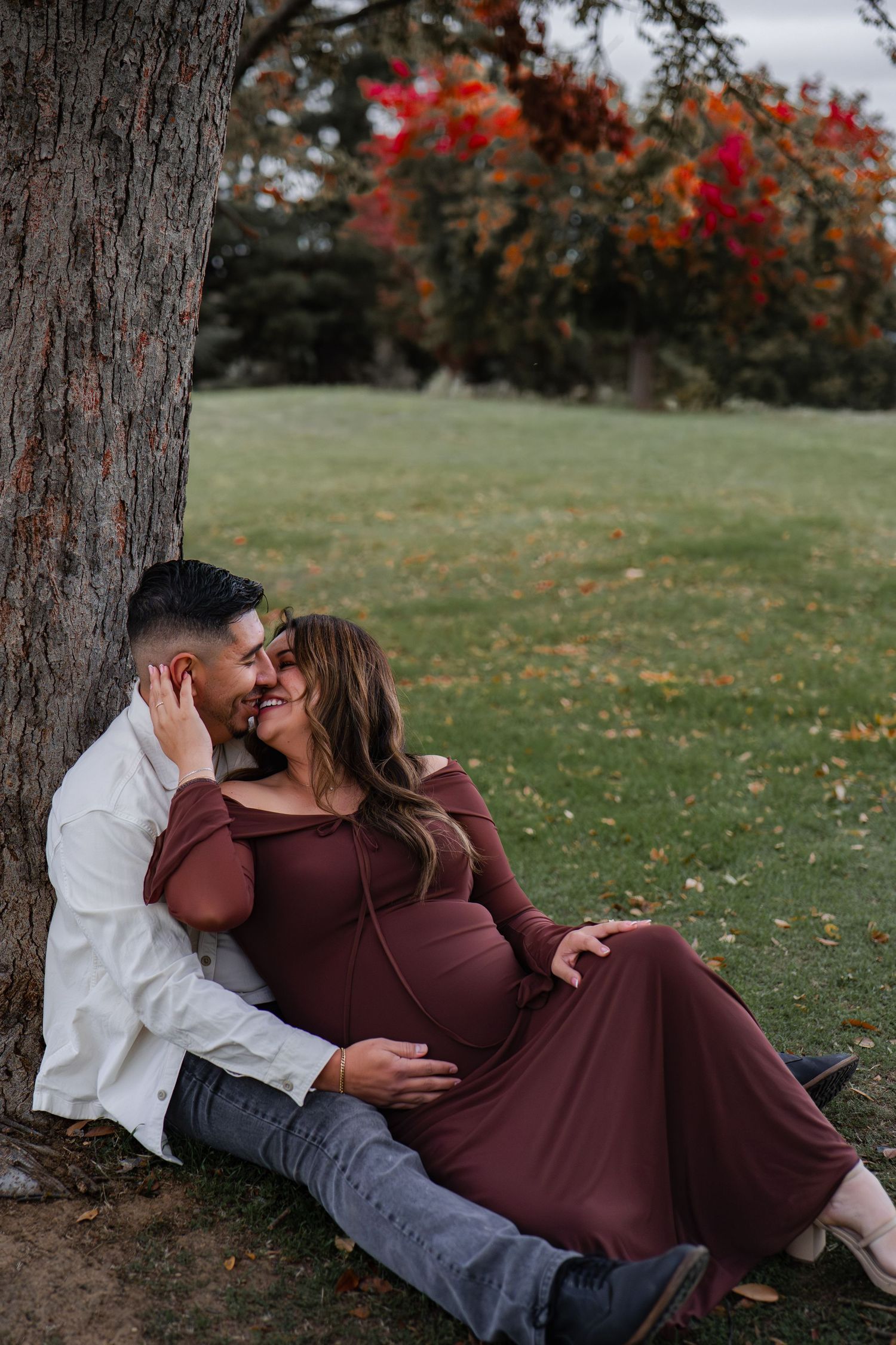 Romantic couple's maternity photos under fall trees with burgundy dress and white shirt in Roseville, CA