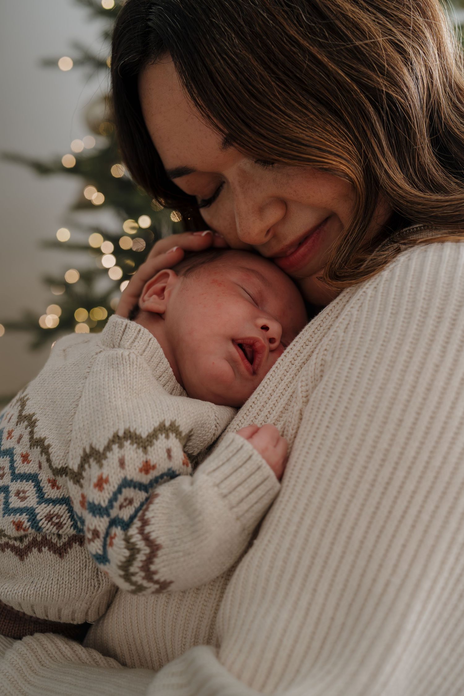 A tender moment shows two people in cozy white sweaters embracing while resting against soft winter lighting.