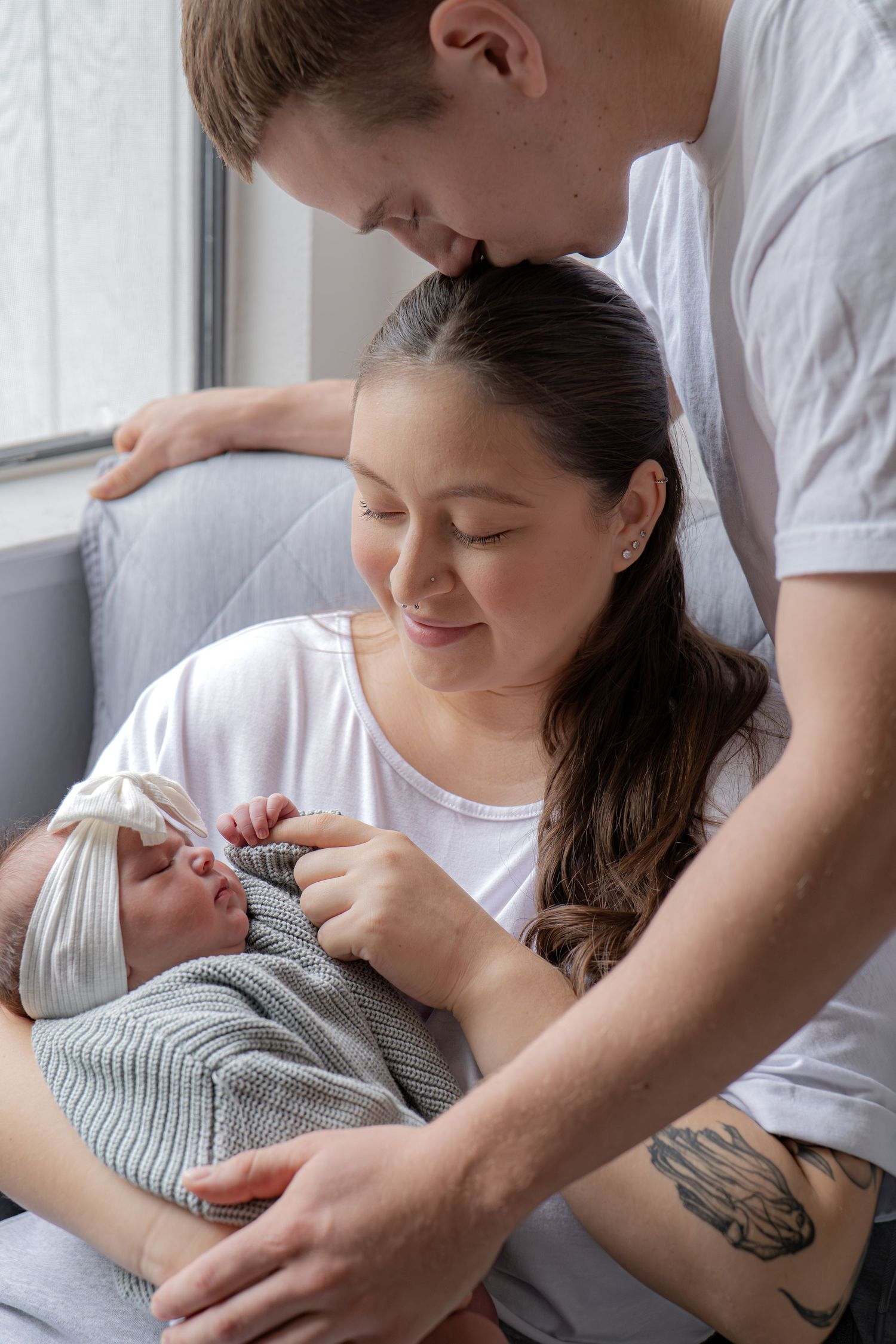 Parents gazing lovingly at their newborn baby wrapped in gray knit blanket.