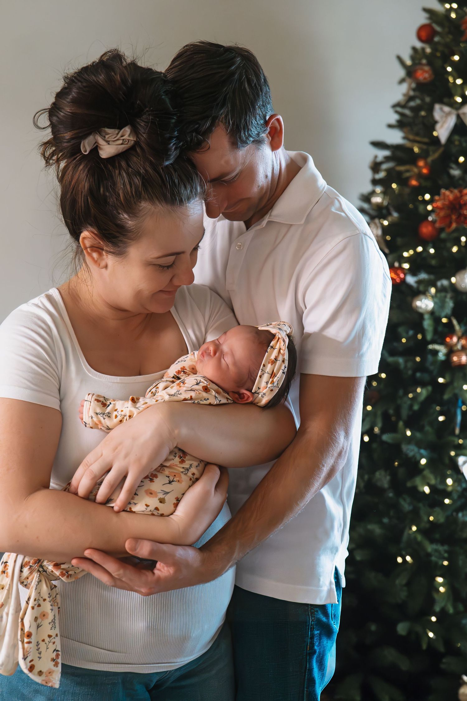 Parents holding their newborn baby near a decorated Christmas tree.