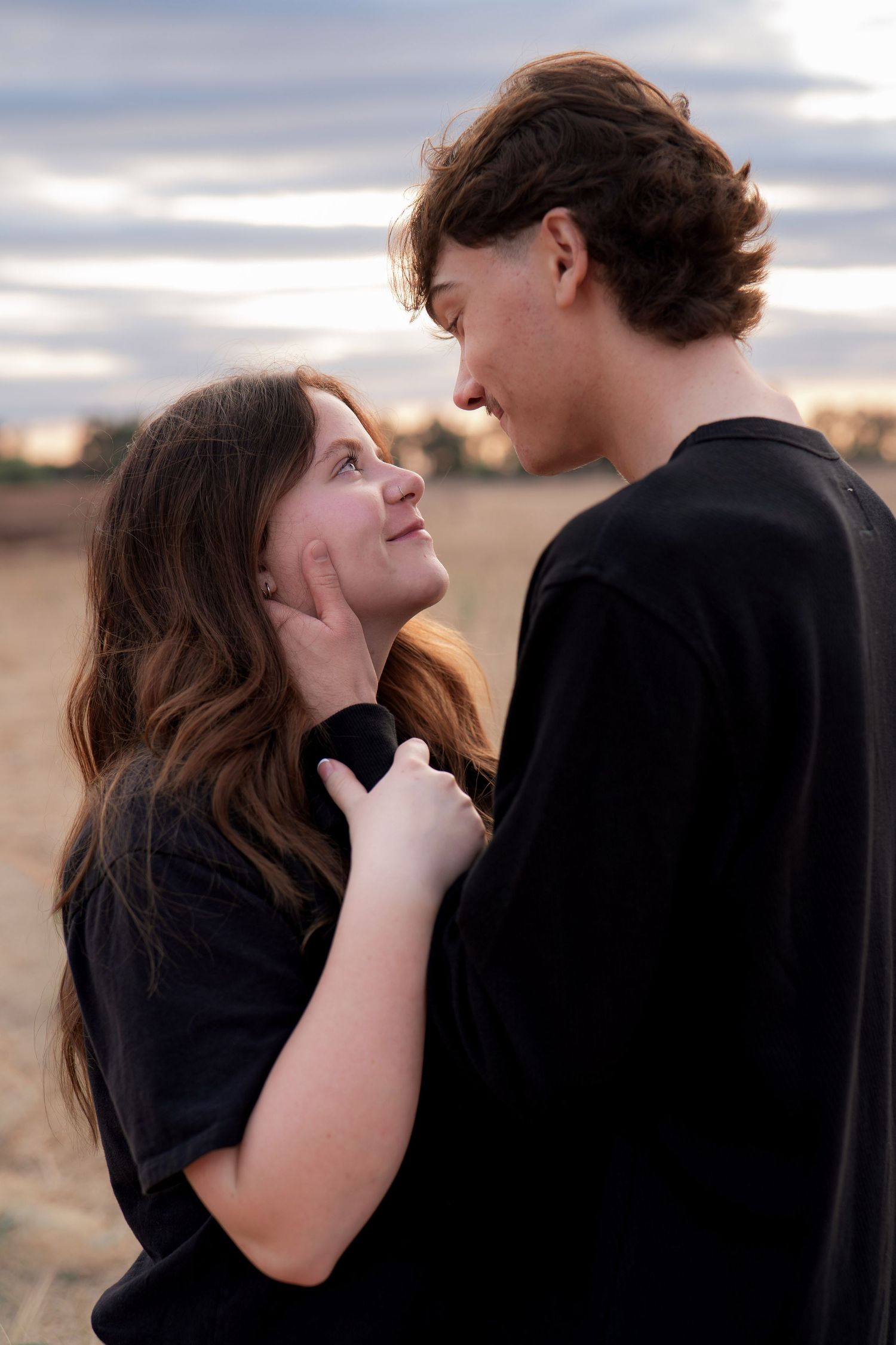 A romantic couple shares an intimate moment against a moody sky backdrop.
