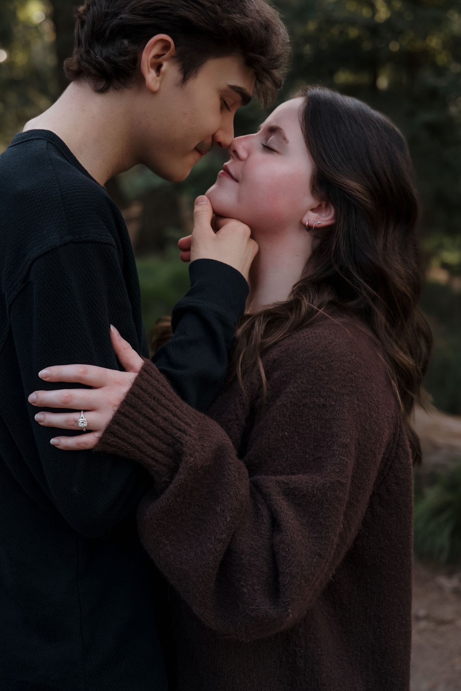 Romantic couple in cozy sweaters sharing an intimate moment outdoors, with the man gently holding the woman's face.