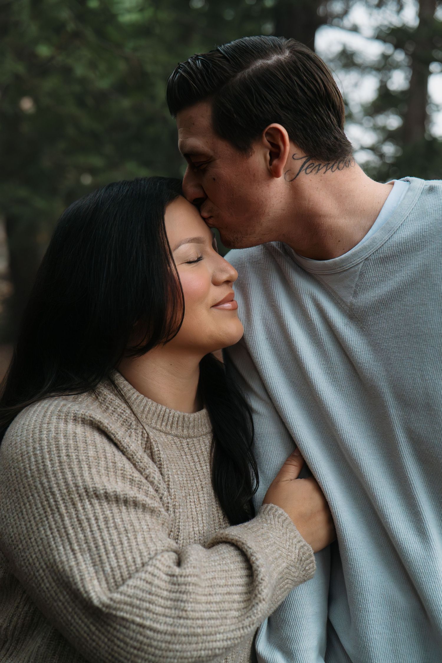 Romantic couple sharing intimate moments in cozy sweaters against forest backdrop in Roseville, CA