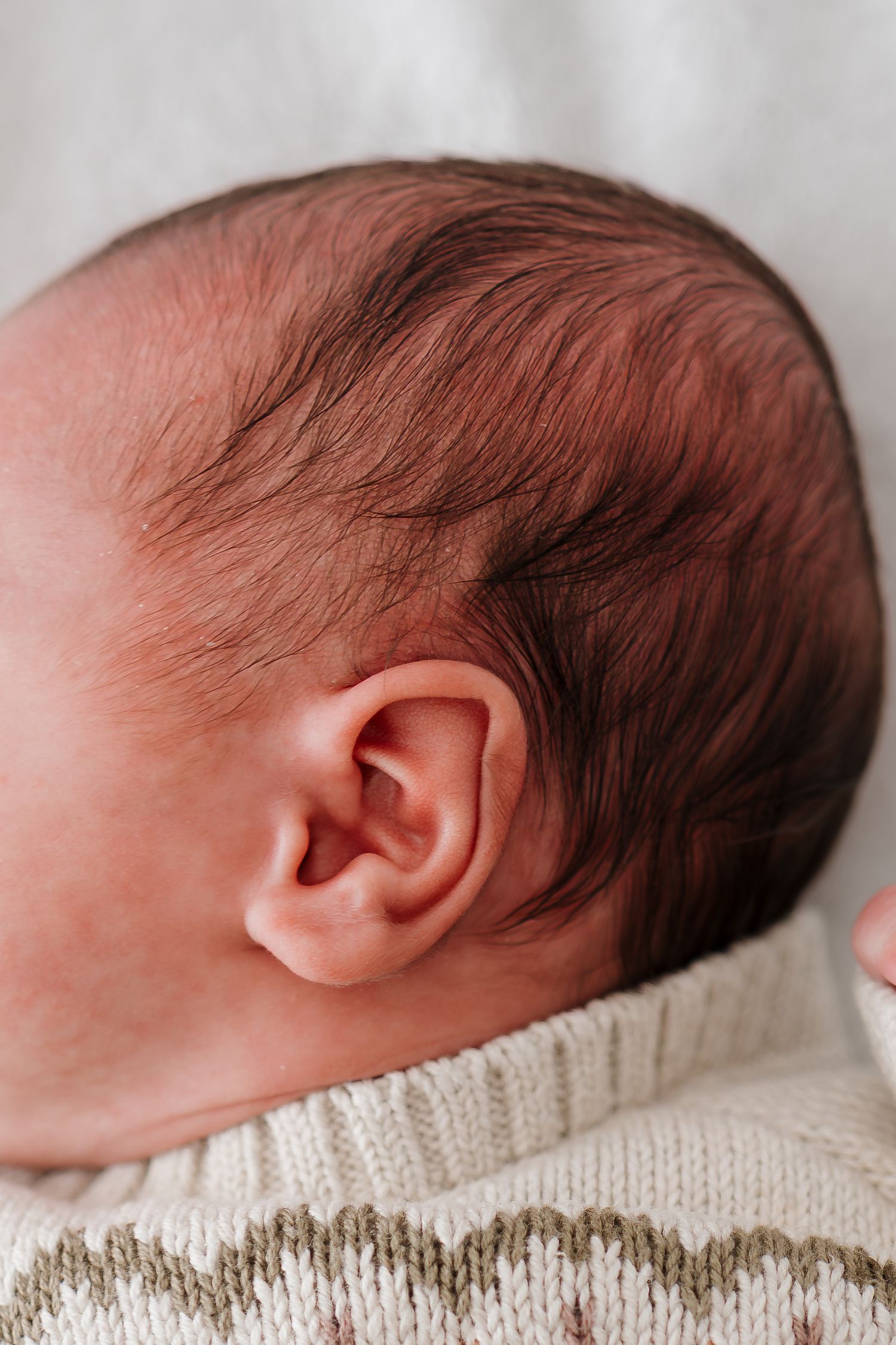 Close-up profile view of a sleeping newborn baby resting on a cream-colored knit blanket.