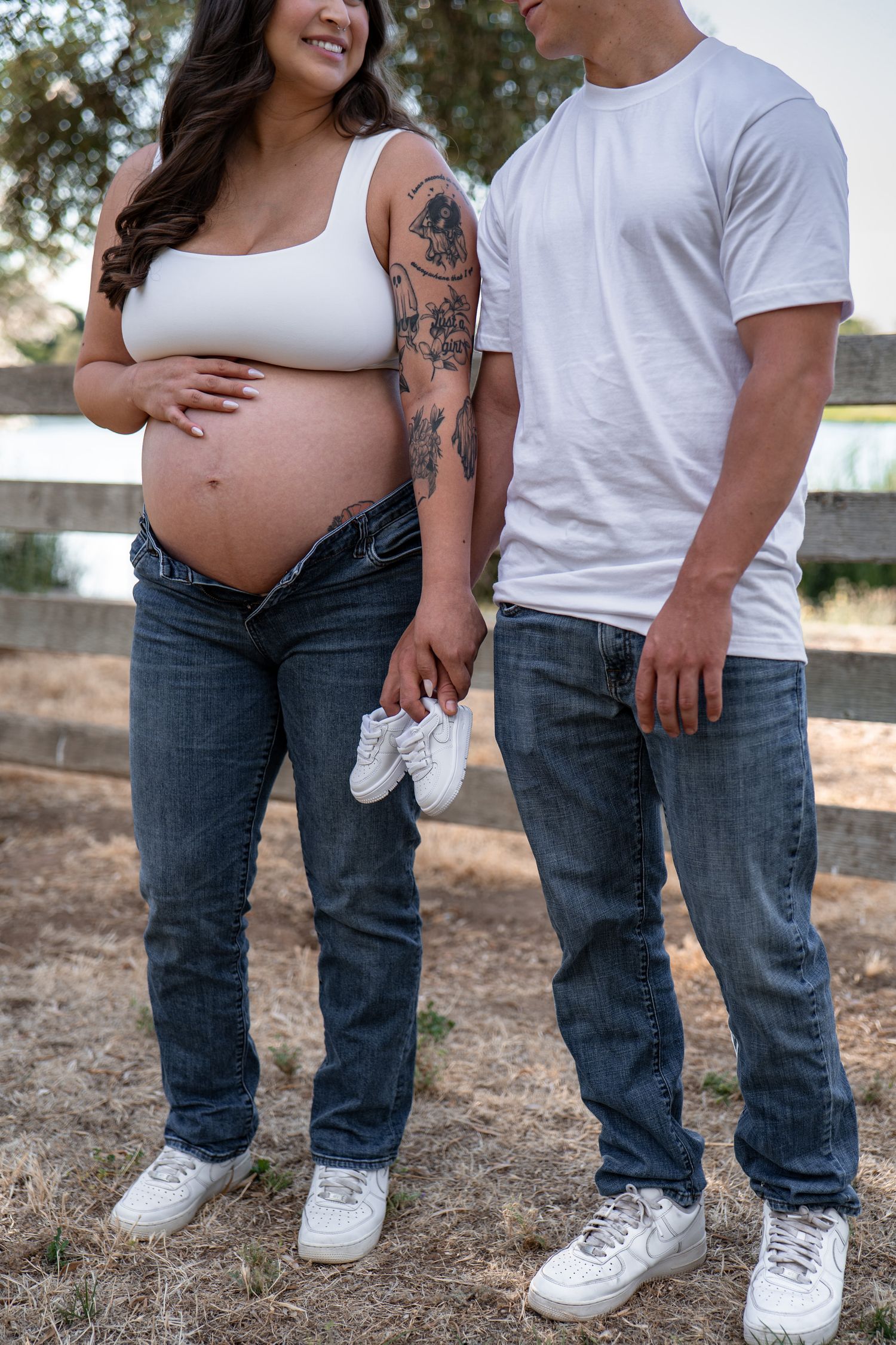 Casual couple in white tops and jeans showing pregnancy journey in outdoor setting.
