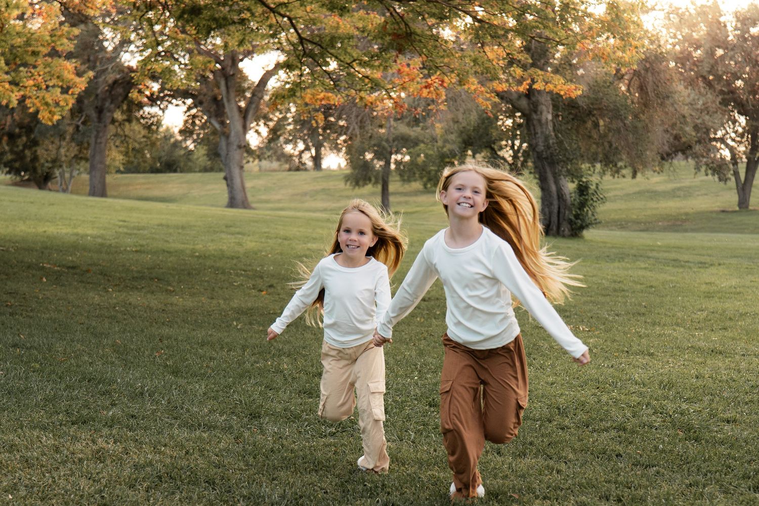 Children run and play in a grassy field during golden hour sunset.