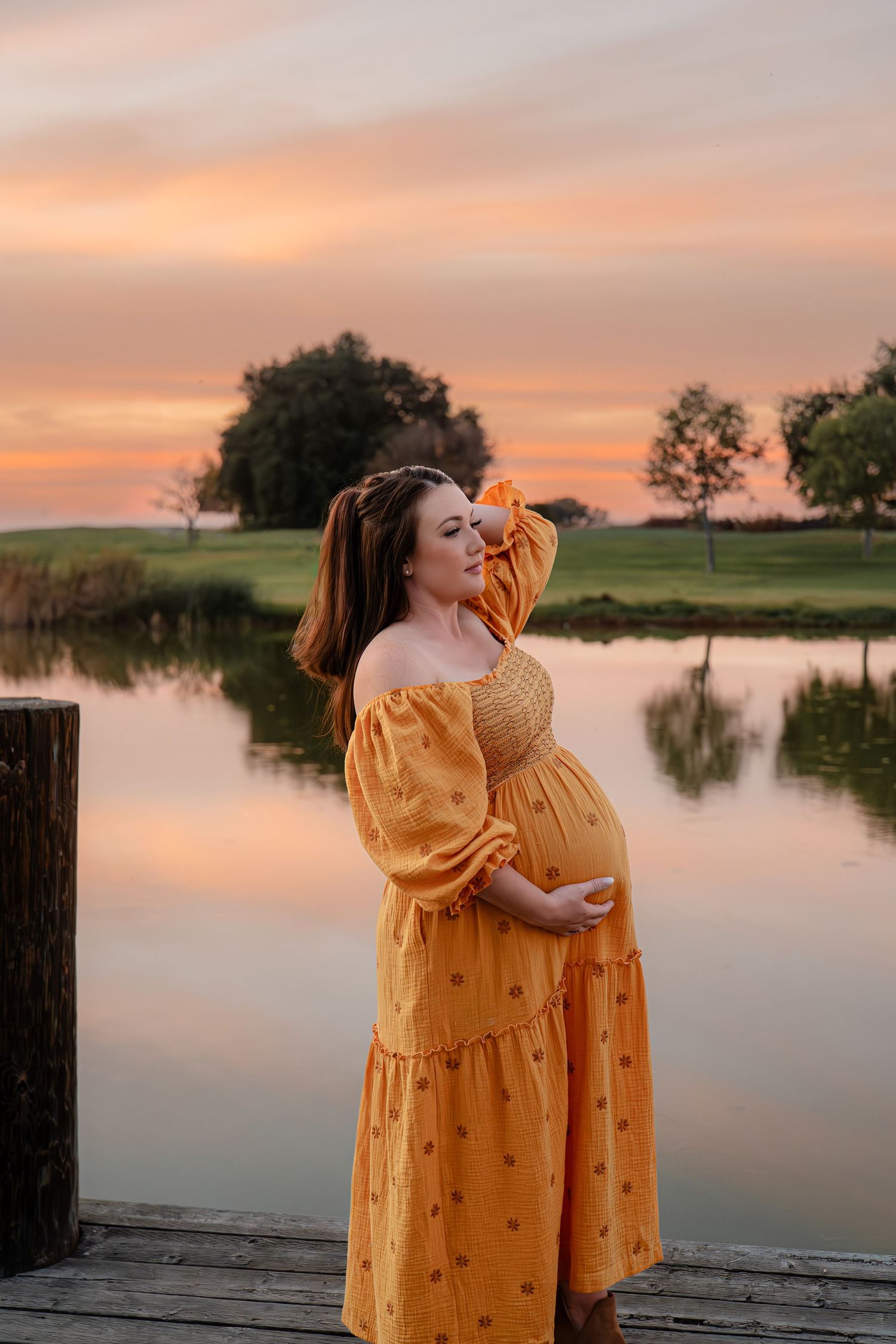 Sunset maternity photos on dock with woman in flowing yellow dress in Roseville, CA