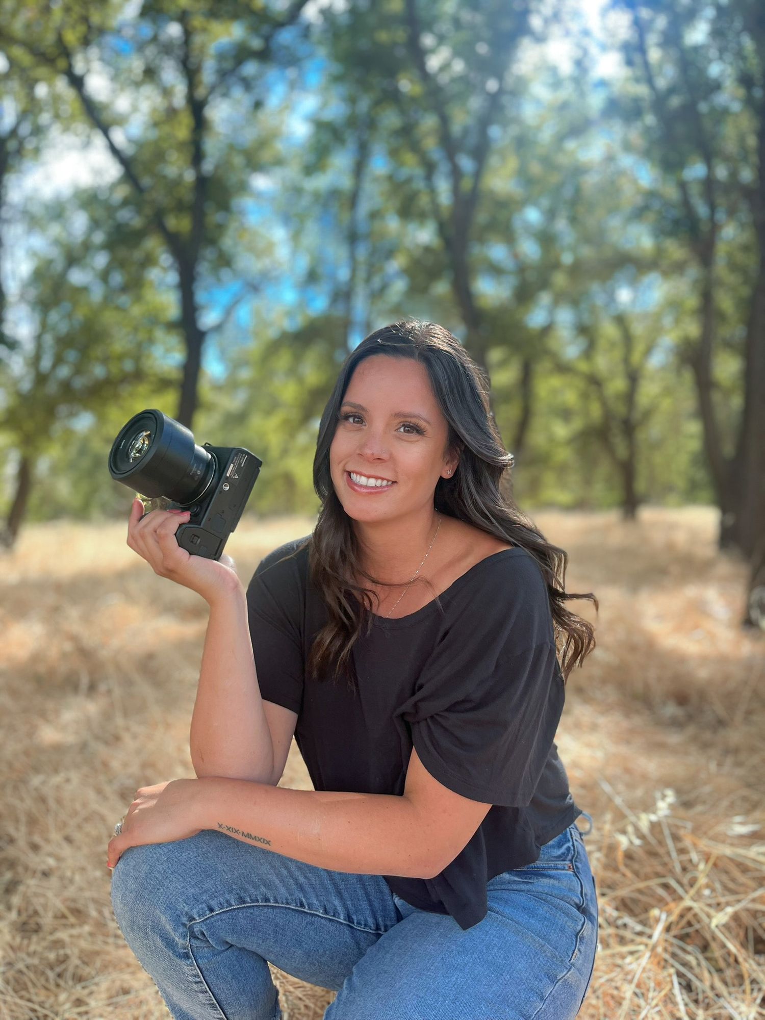 Photographer lying in dry grass holding camera equipment during outdoor photoshoot.