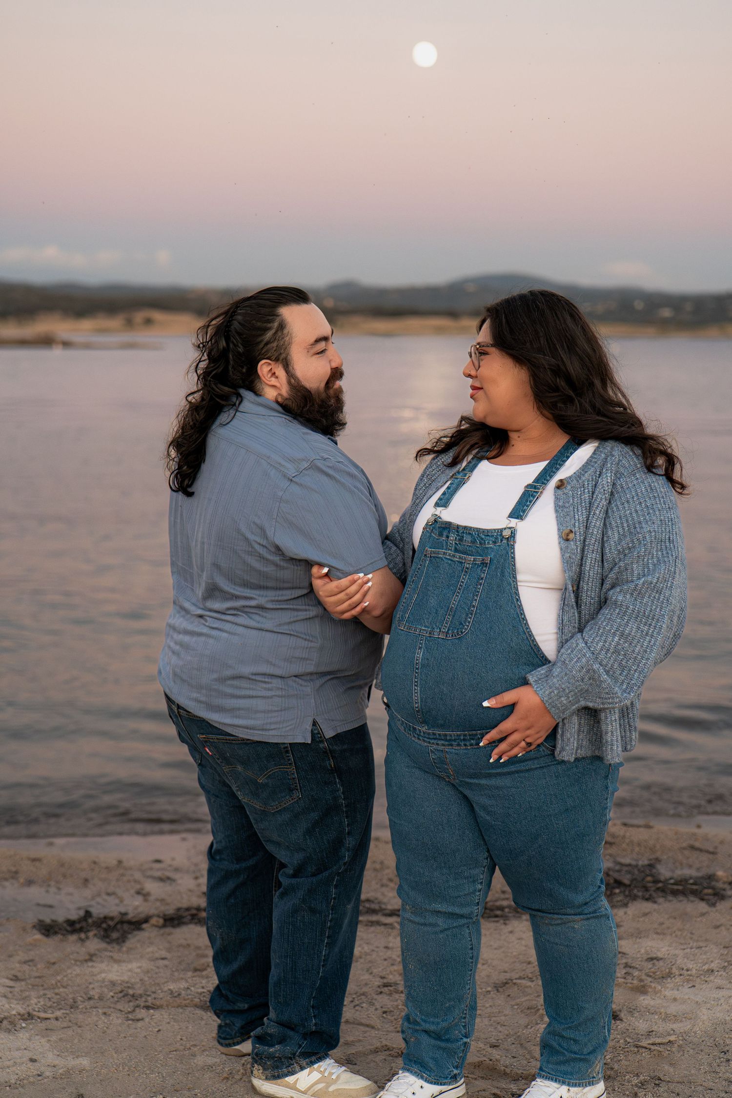 A couple in matching denim and gray outfits share tender moments on a beach at sunset.