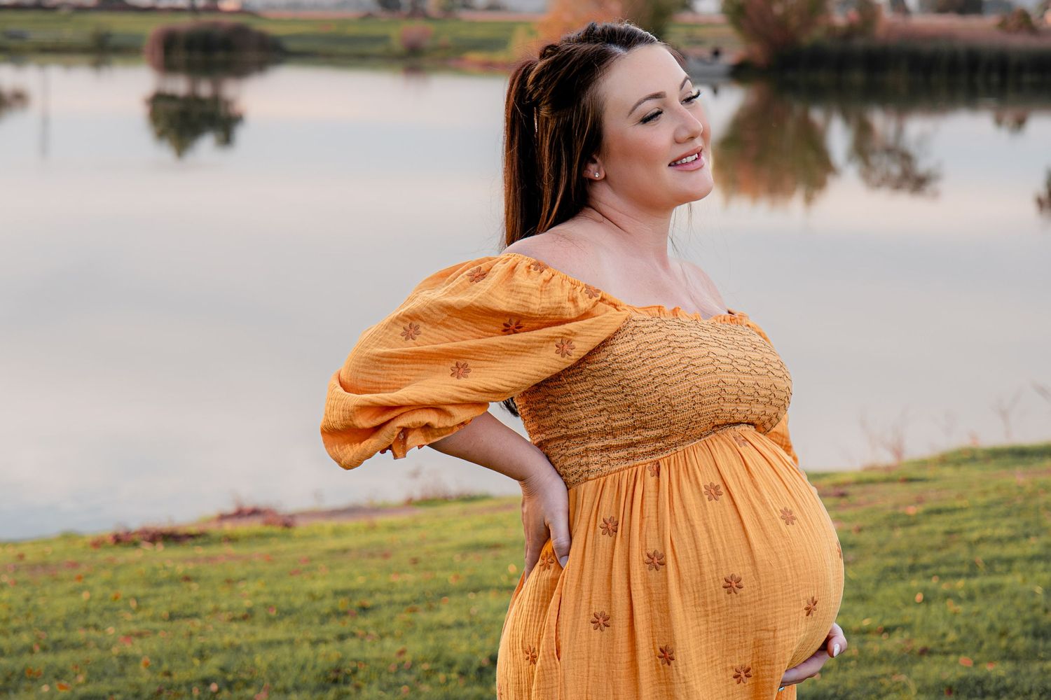 Pregnant woman in flowing yellow dress poses outdoors at sunset in Roseville, CA