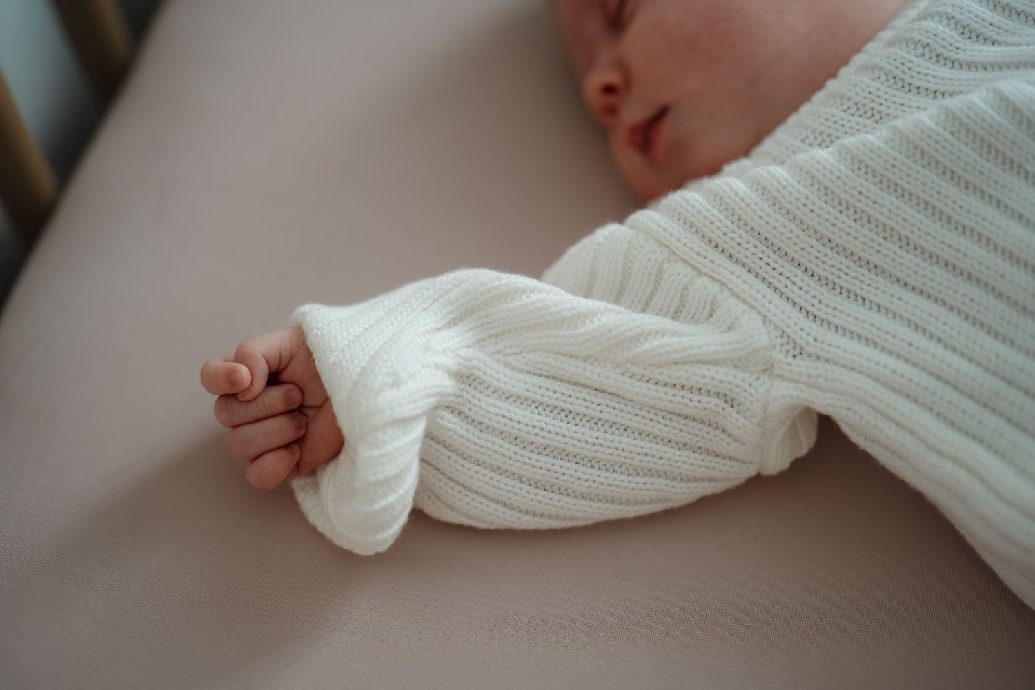 Baby resting peacefully in soft white knitted clothing against neutral background in Roseville, CA