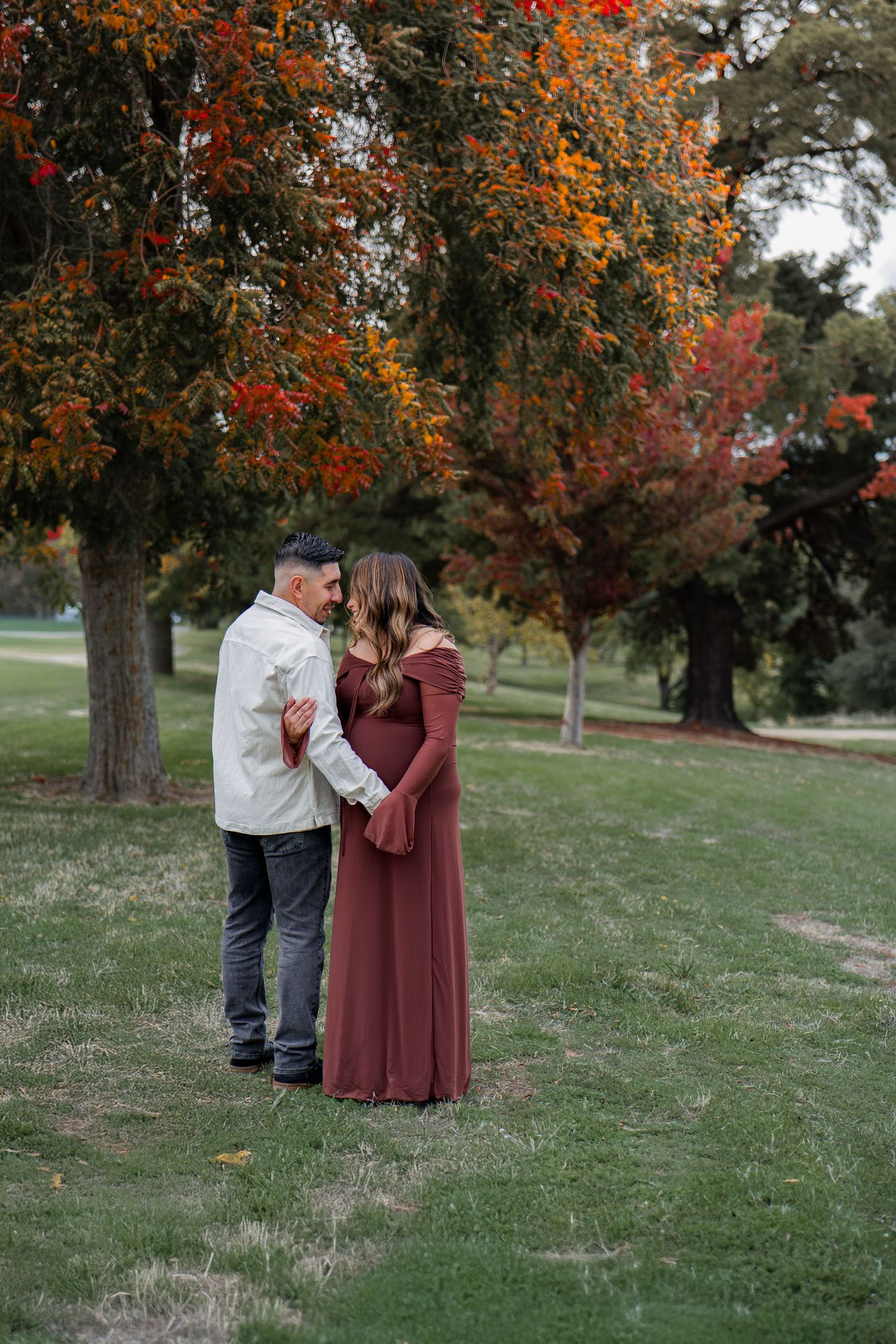 Couple embracing under fall foliage with orange and red leaves.