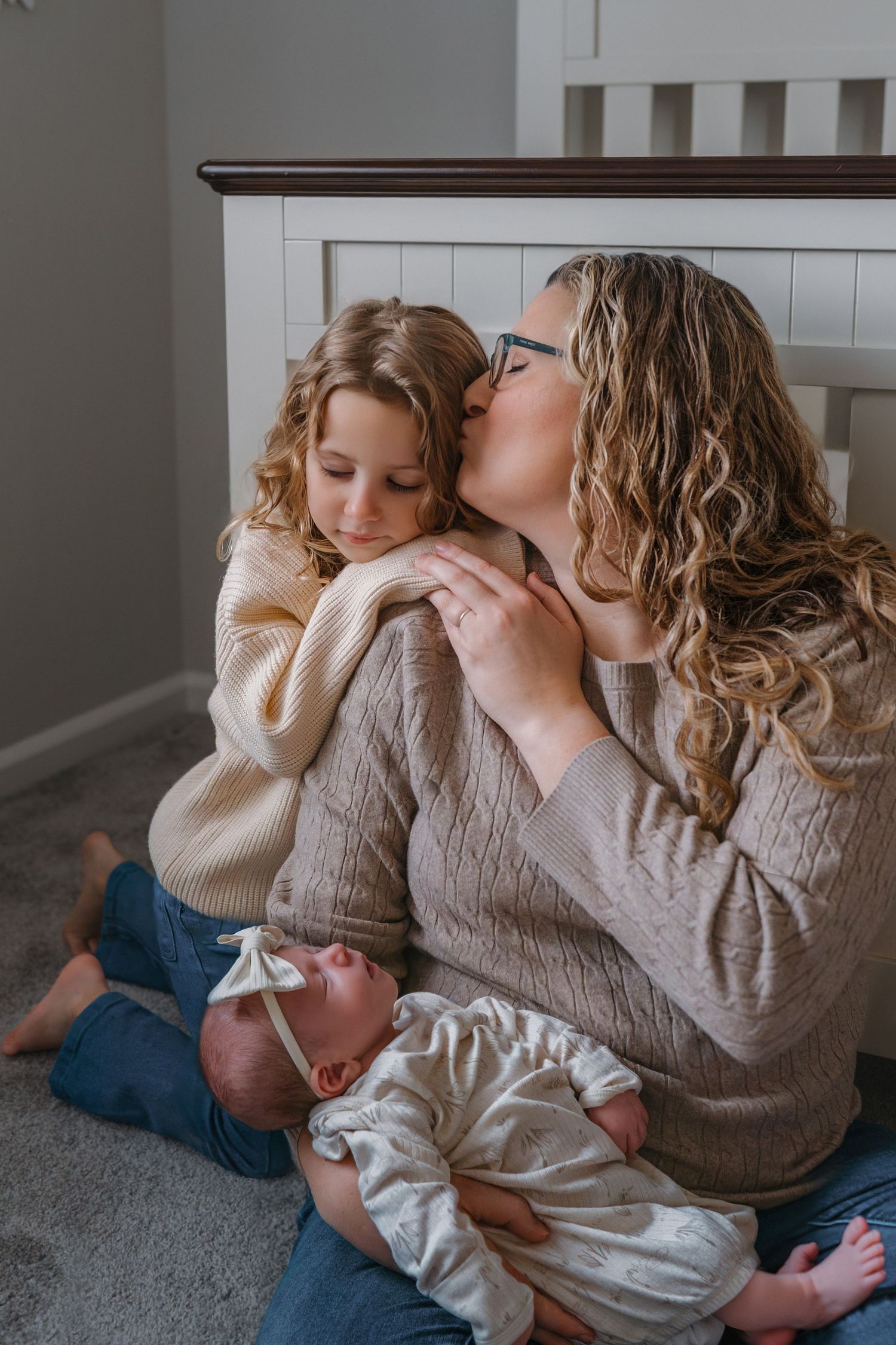 A tender moment between parent and child laying together on a carpeted floor in soft neutral colored clothing.