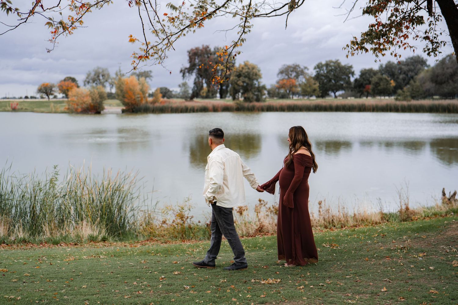 Family walking along a serene lakeside path during autumn with tall grass in the background in Roseville, CA