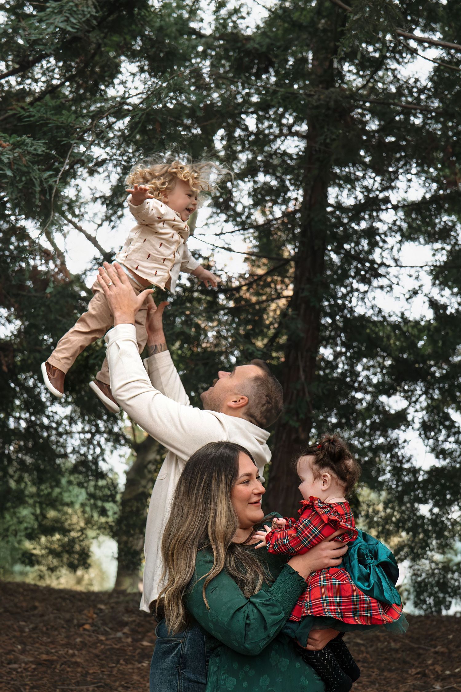 Playful family moment captured in forest setting with natural light filtering through trees in Roseville, CA